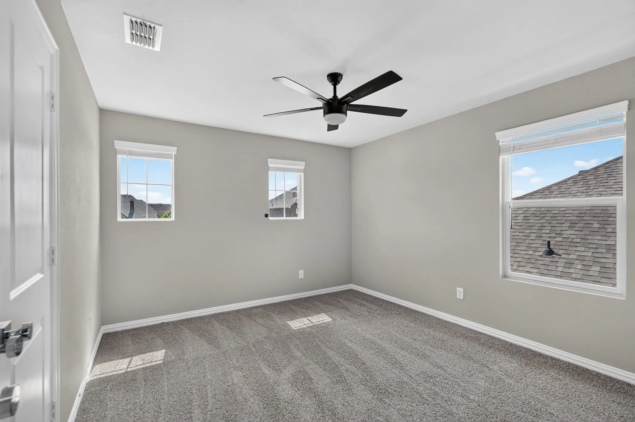 Neutral paint palette, dark carpet, multiple windows with blinds, ceiling fan, and paneled interior door