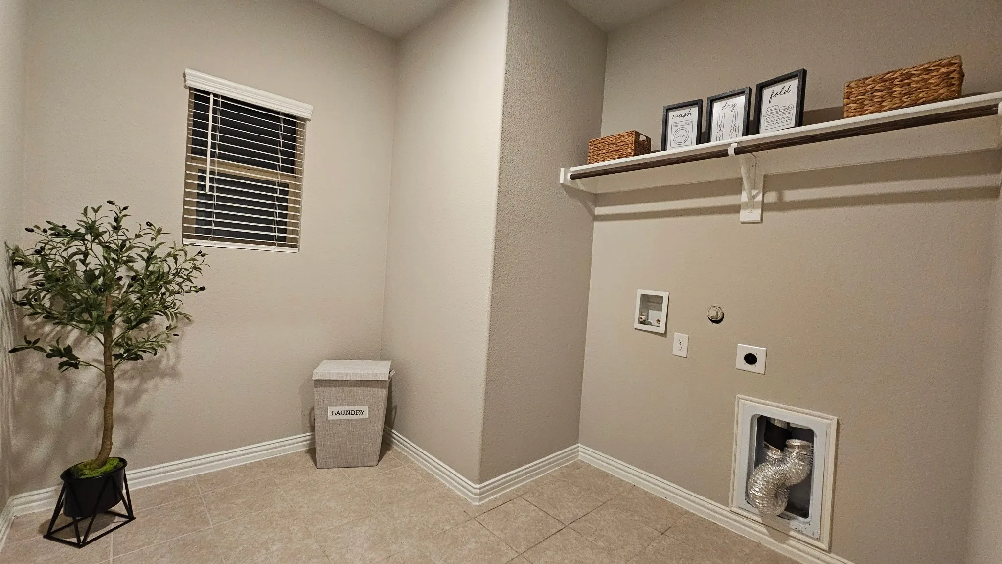 Utility room featuring tile flooring, a window with blinds, and a built-in shelf with a clothing rod