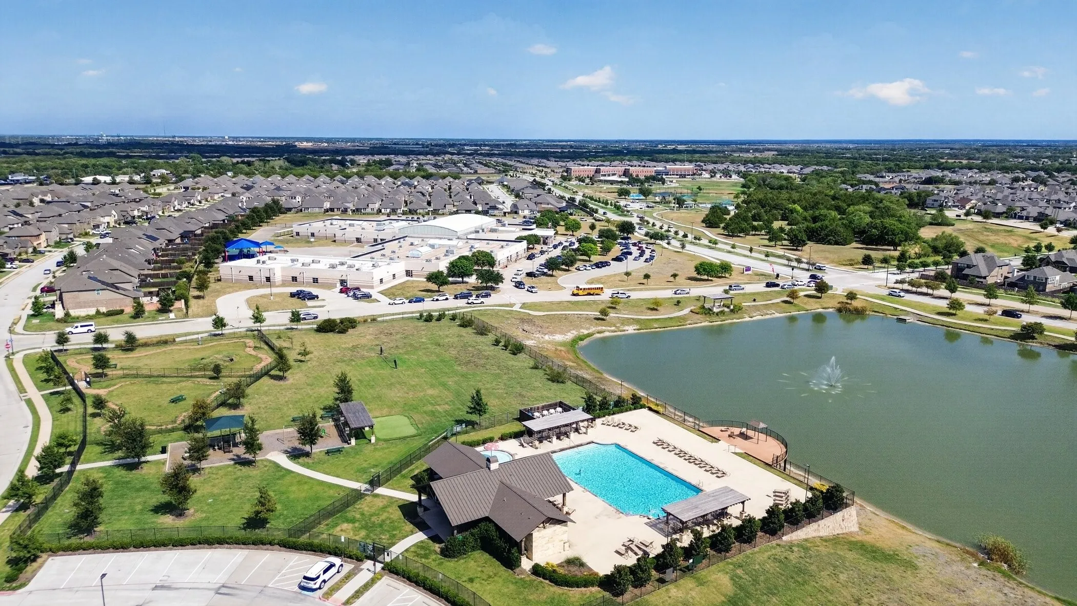 Community features a large swimming pool with surrounding lounge areas, a shaded pavilion, and an adjacent water body with a fountain