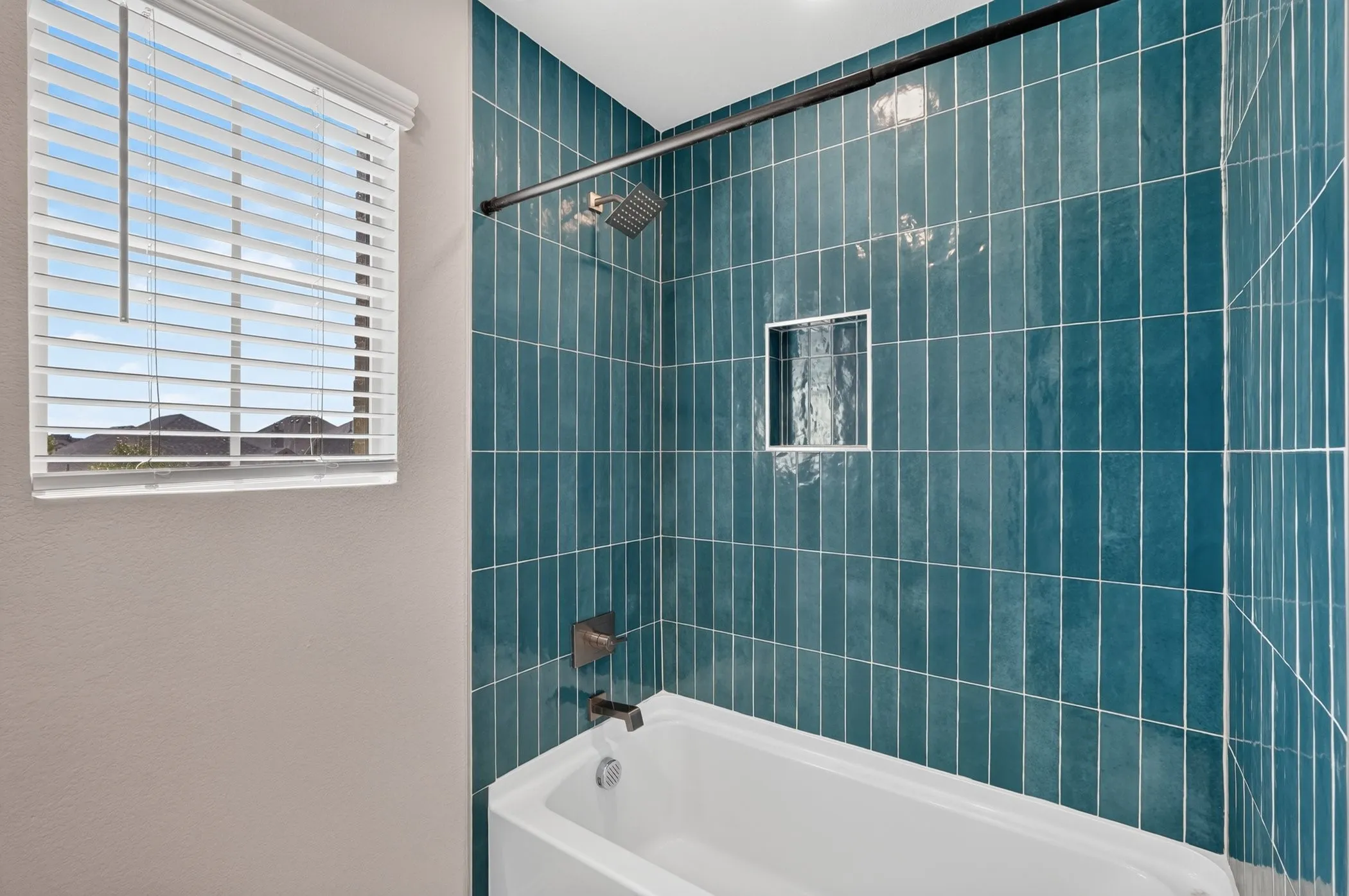 Tub and shower combination featuring teal tile surround, built-in niche, and matte black shower rod