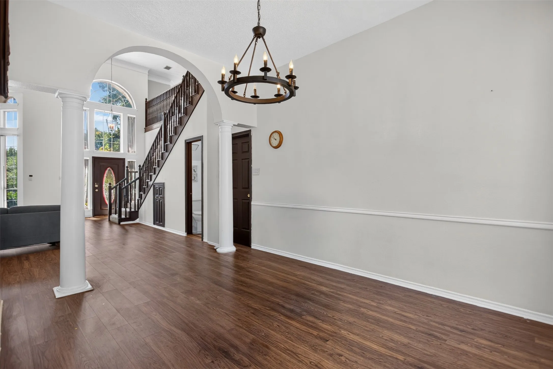 Wood-finish flooring throughout, archway entry, and a prominent staircase with dark wood handrails