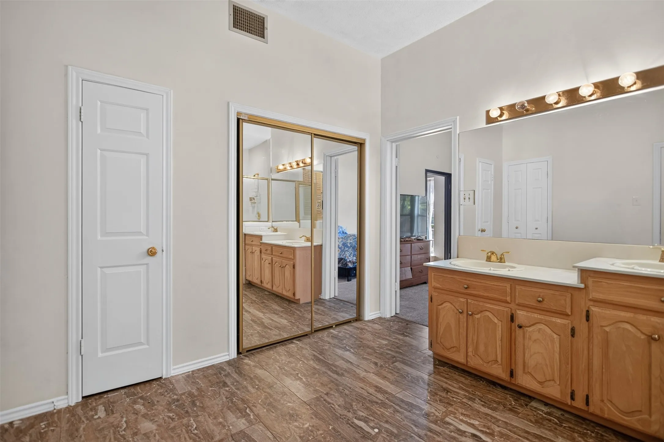 Dual vanity with integrated sinks, wood-finish cabinetry, and a large mirror with a multi-bulb light fixture