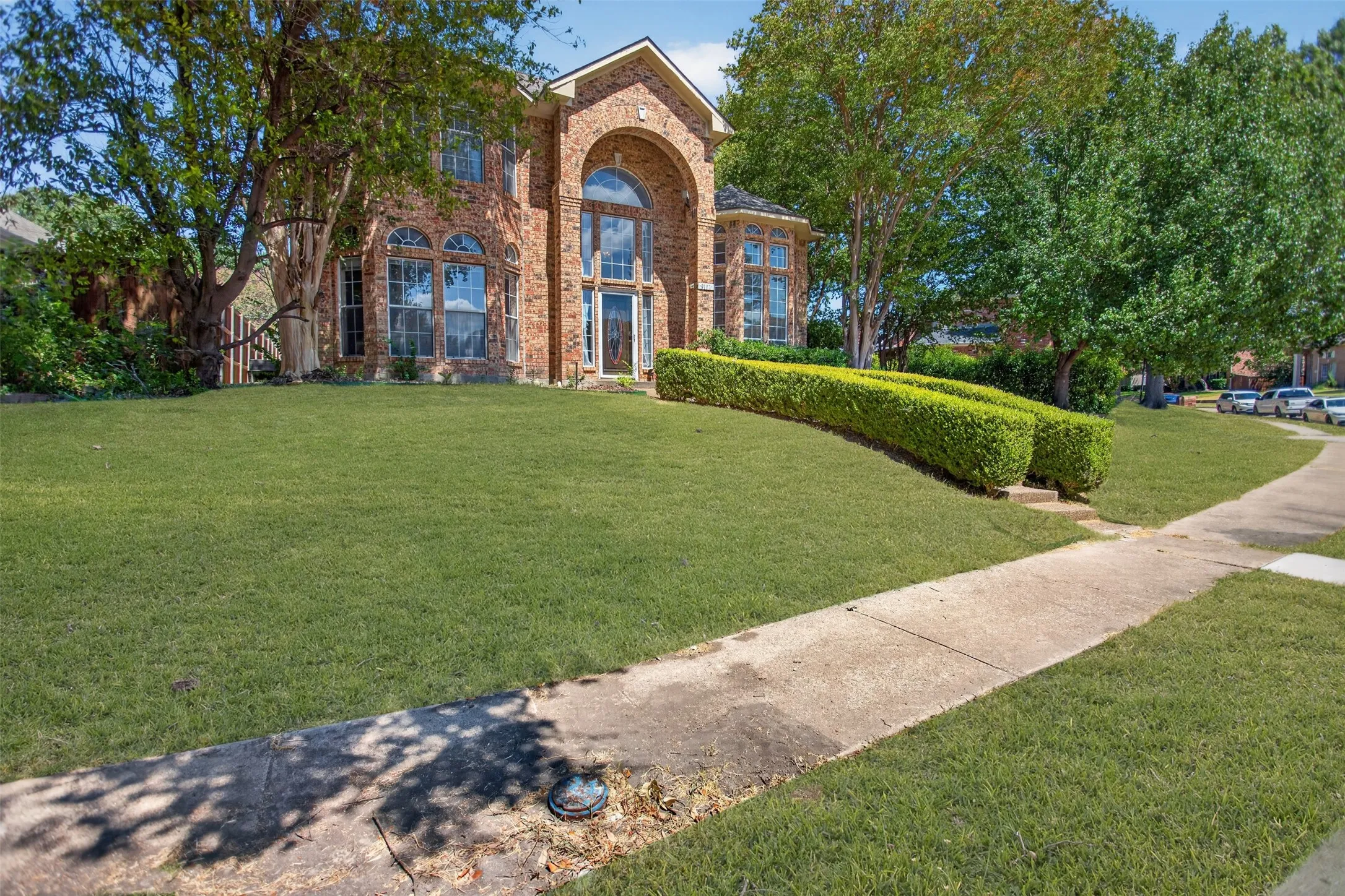 Brick exterior with arched entryway, large bay window, and a spacious front lawn featuring manicured hedges