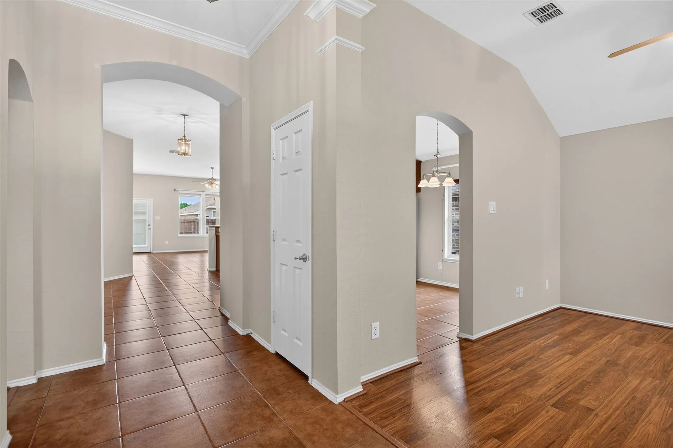Arched doorways, vaulted ceiling, crown molding, tile flooring, and wood-finish flooring