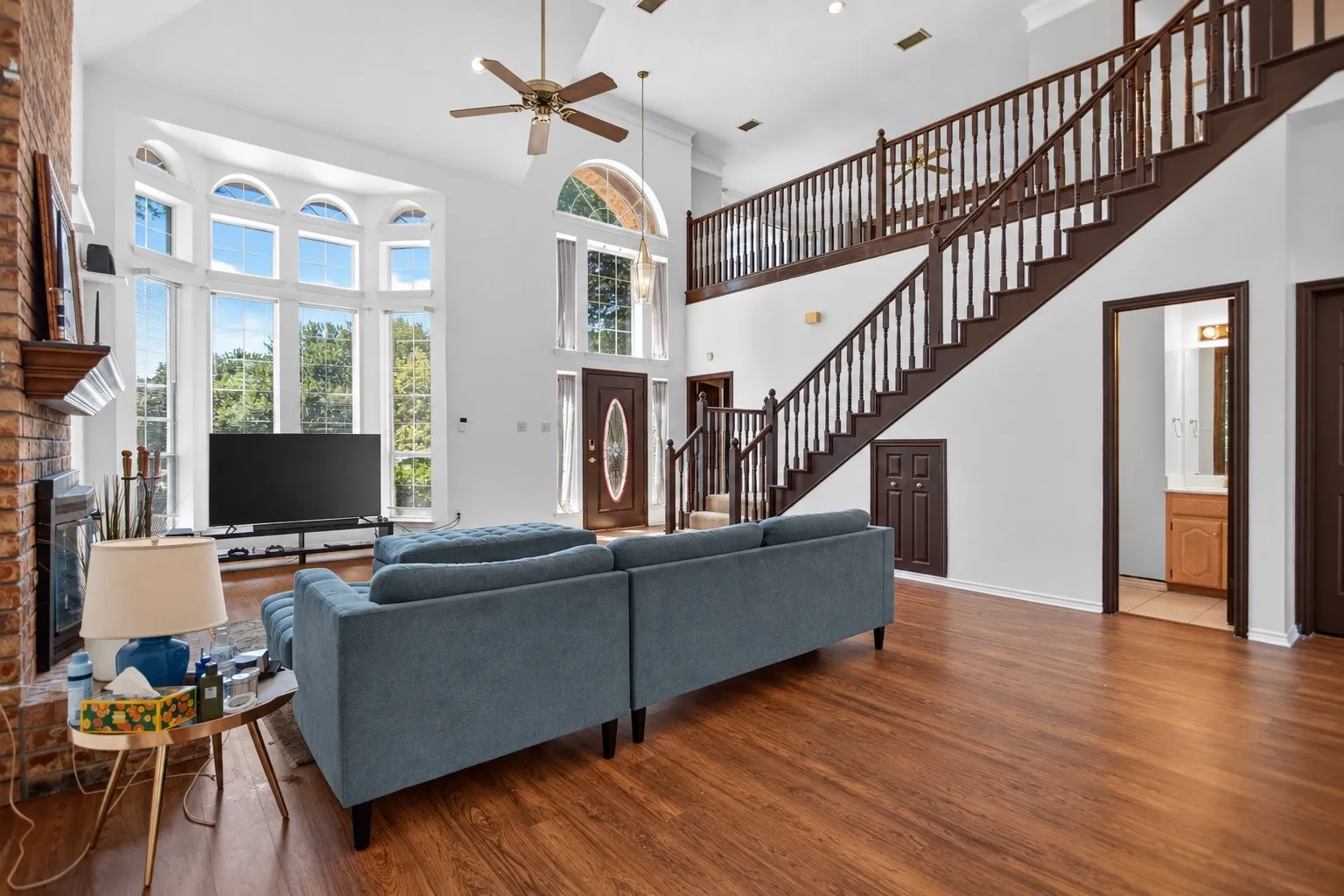 Two-story living area with vaulted ceilings, a brick fireplace, wood-finish flooring, a grand staircase, and an upper-level balcony