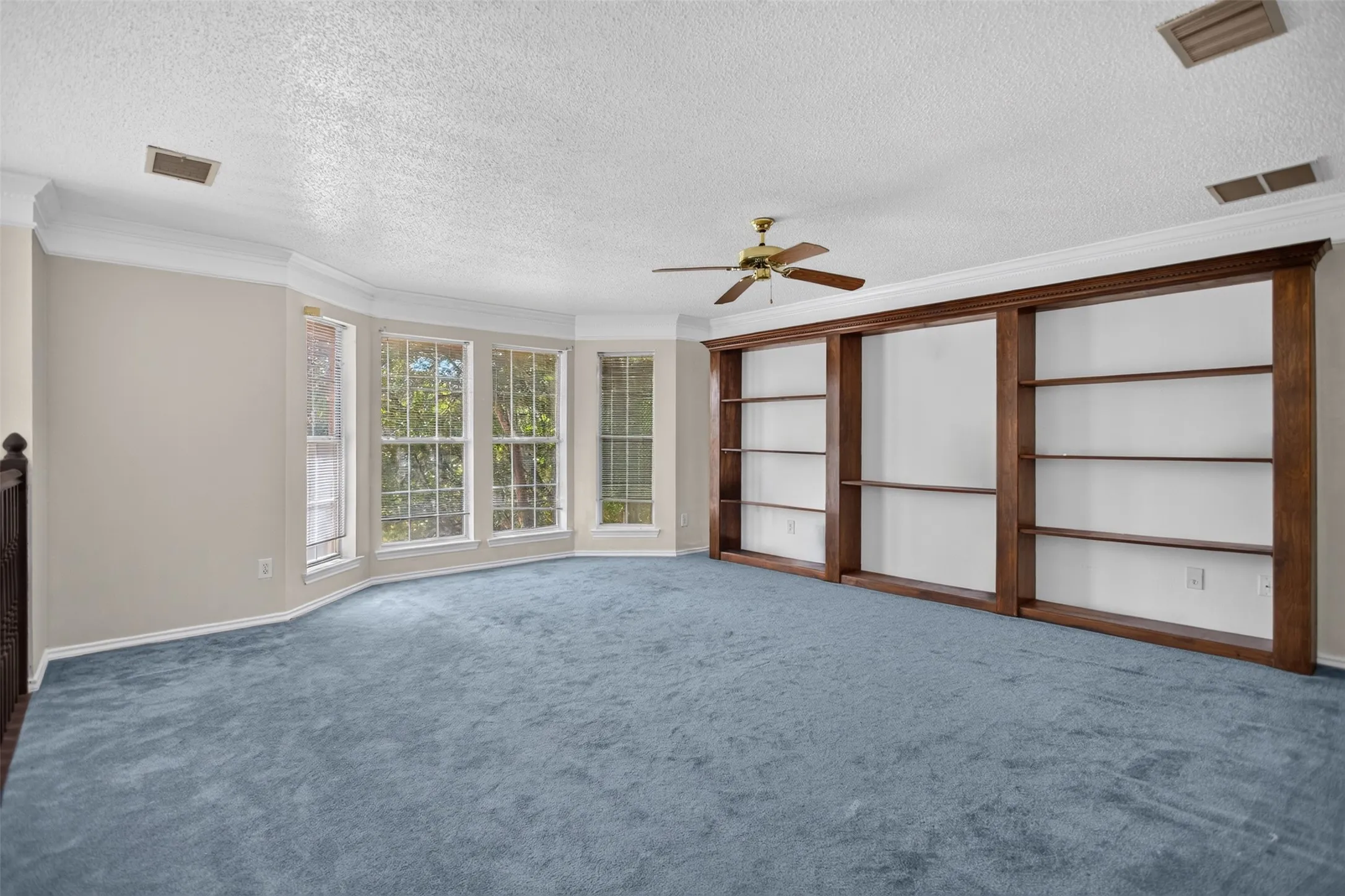 Expansive room featuring a bay window, built-in shelving, crown molding, and a ceiling fan