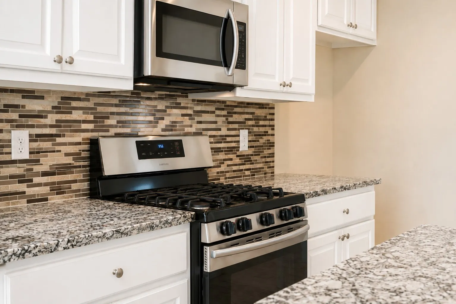 White cabinetry with brushed nickel hardware, stainless steel microwave, mosaic tile backsplash, gas range, and speckled countertops