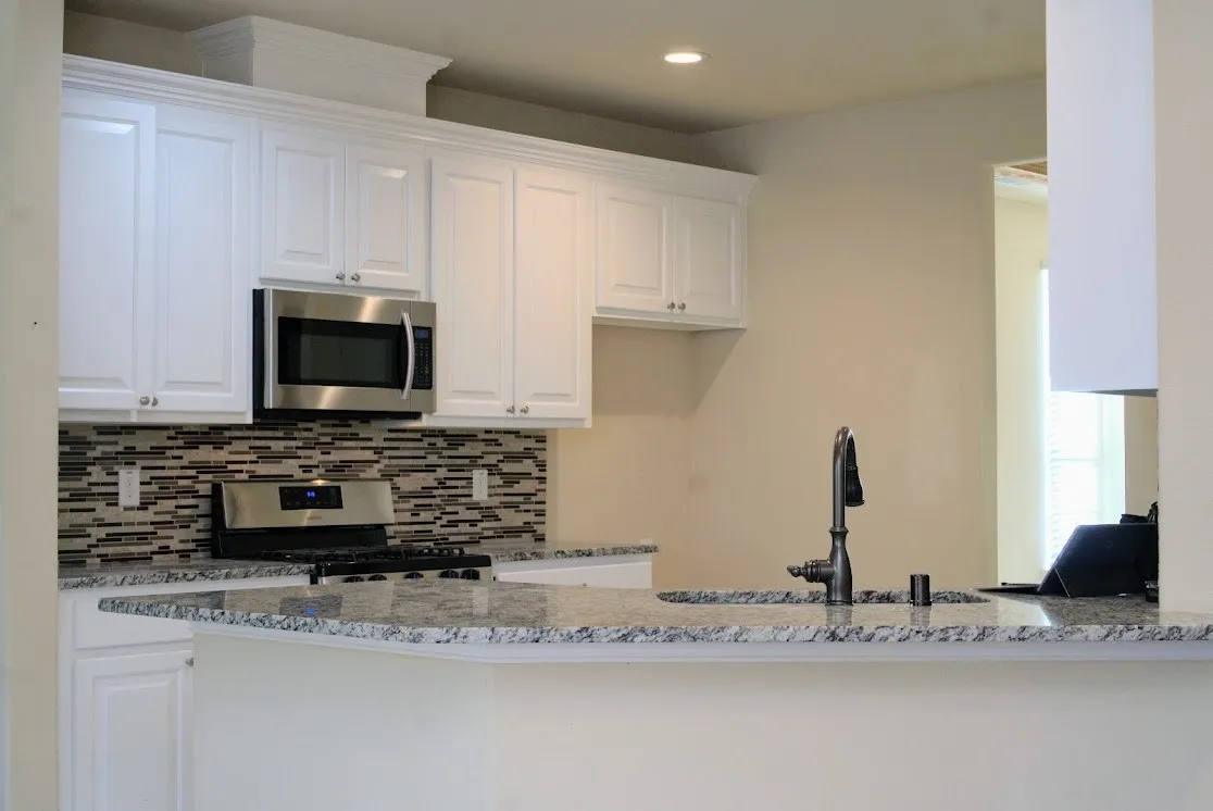 White shaker cabinetry, stainless steel appliances, mosaic tile backsplash, granite countertops, and a gooseneck faucet