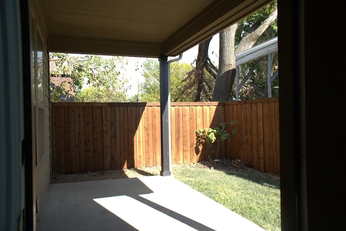 Covered patio with concrete flooring, wood privacy fence, and a grass area