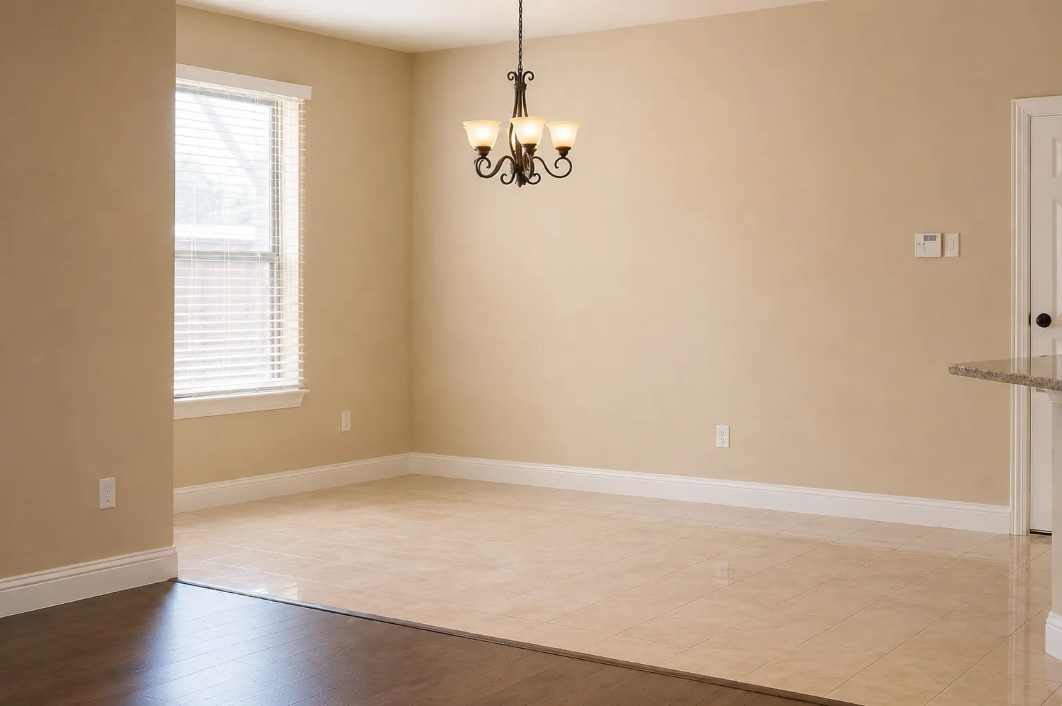 Expansive room featuring a tiered chandelier, window with blinds, tile flooring, and a partial granite countertop