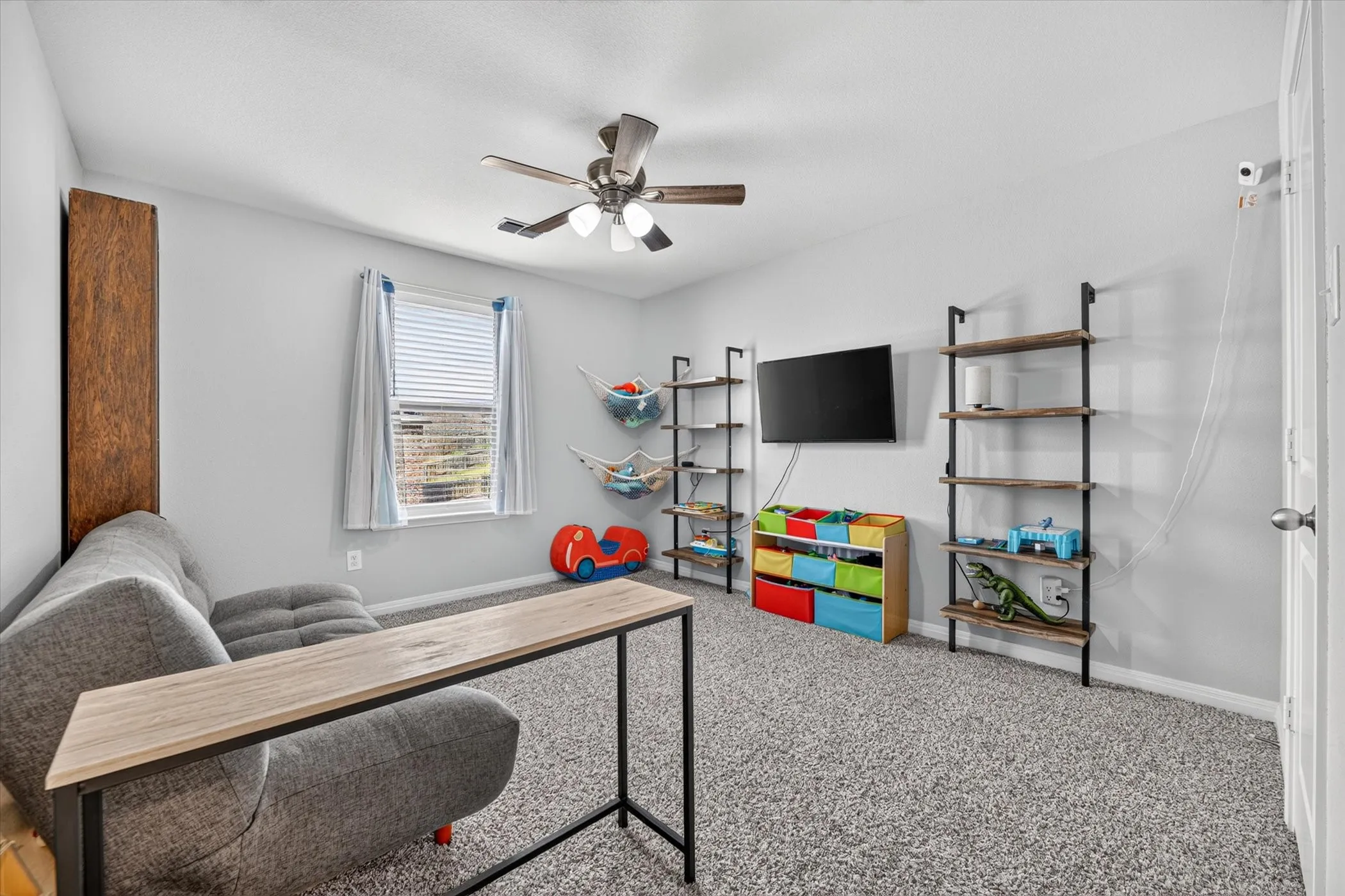 Carpeted room with a ceiling fan, a window with blinds, and built-in shelving units