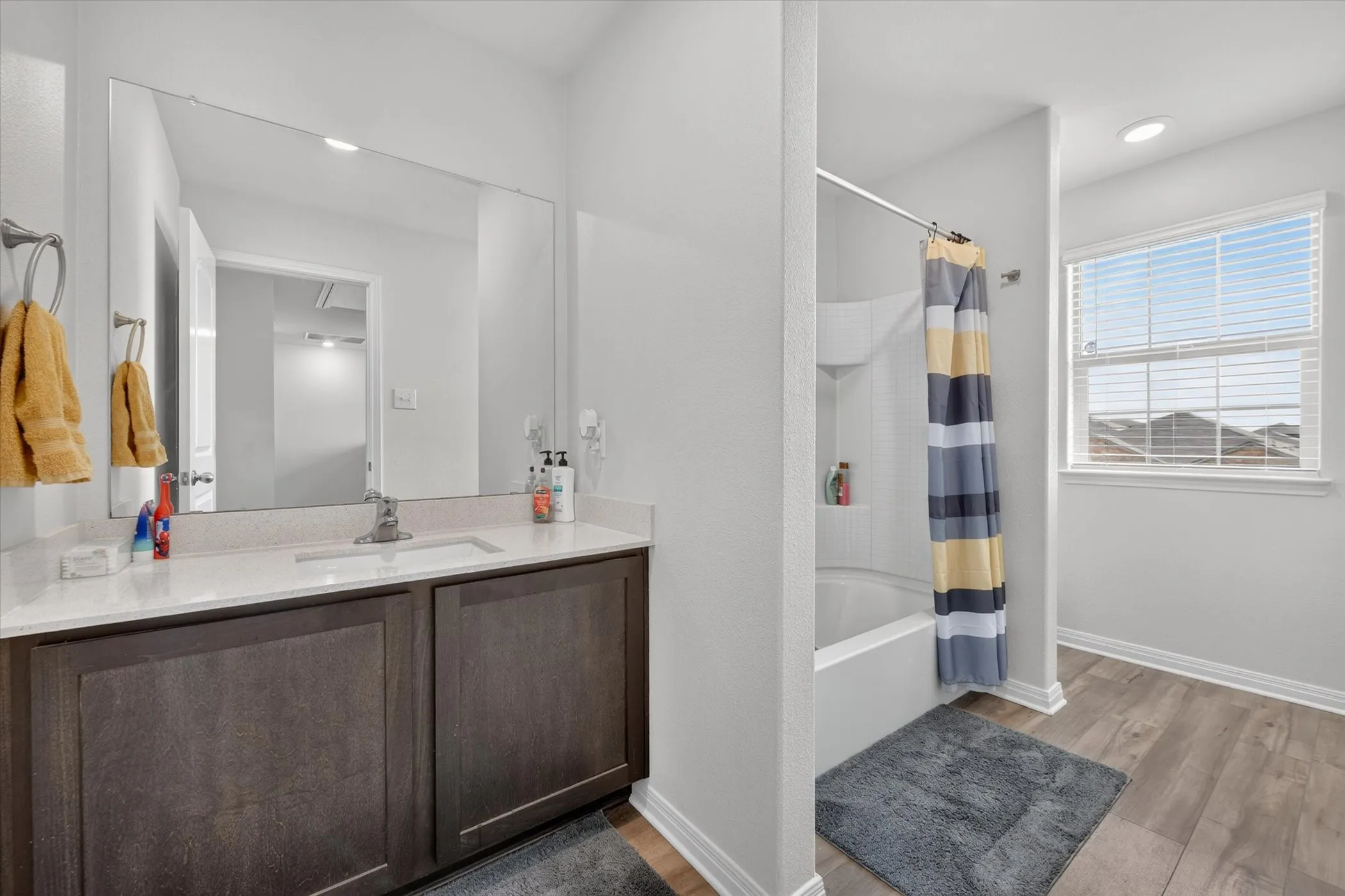 Bathroom featuring a vanity with an integrated sink, broad wall-mounted mirror, wood-finish flooring, and a window