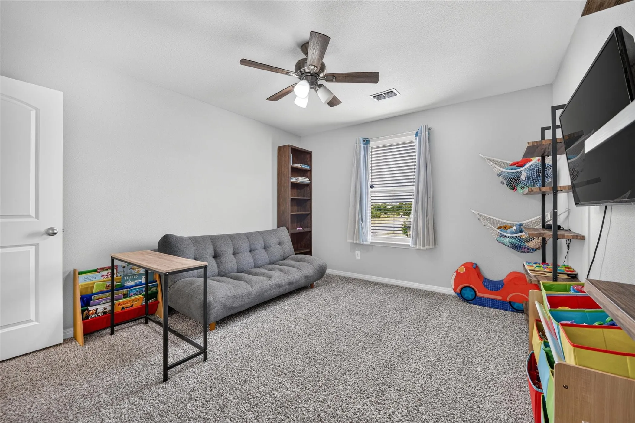 Carpeted room with a ceiling fan, a window with blinds, and a built-in shelving unit