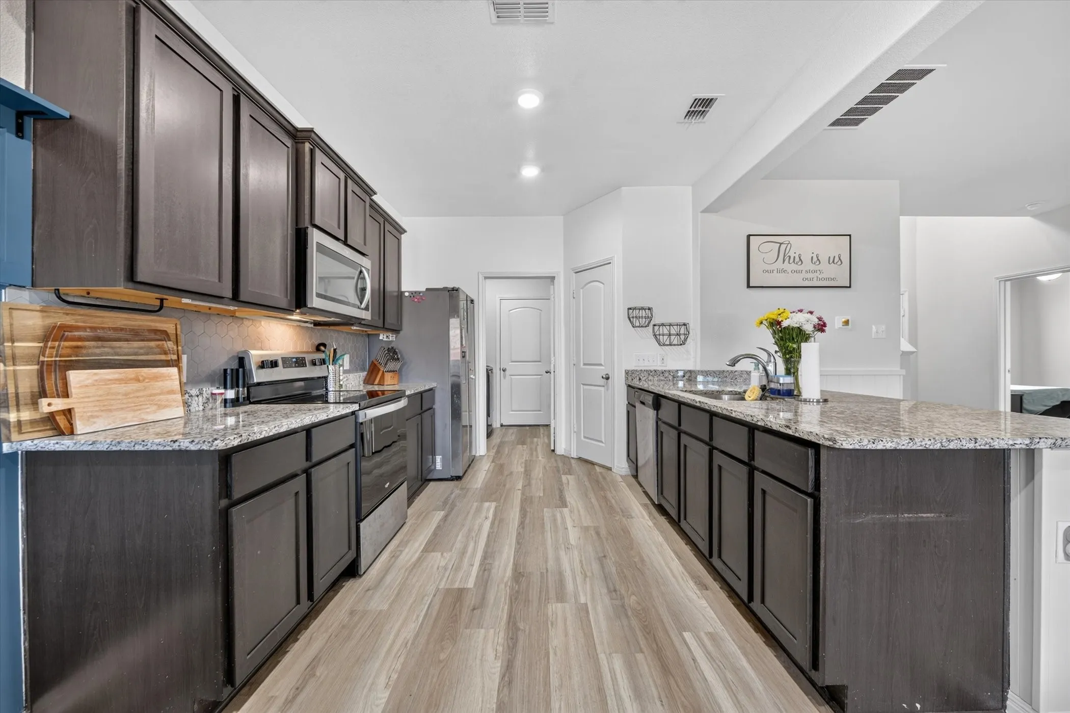 Spacious kitchen featuring wood-finish flooring, dark wood cabinetry, light-toned countertops, and stainless steel appliances