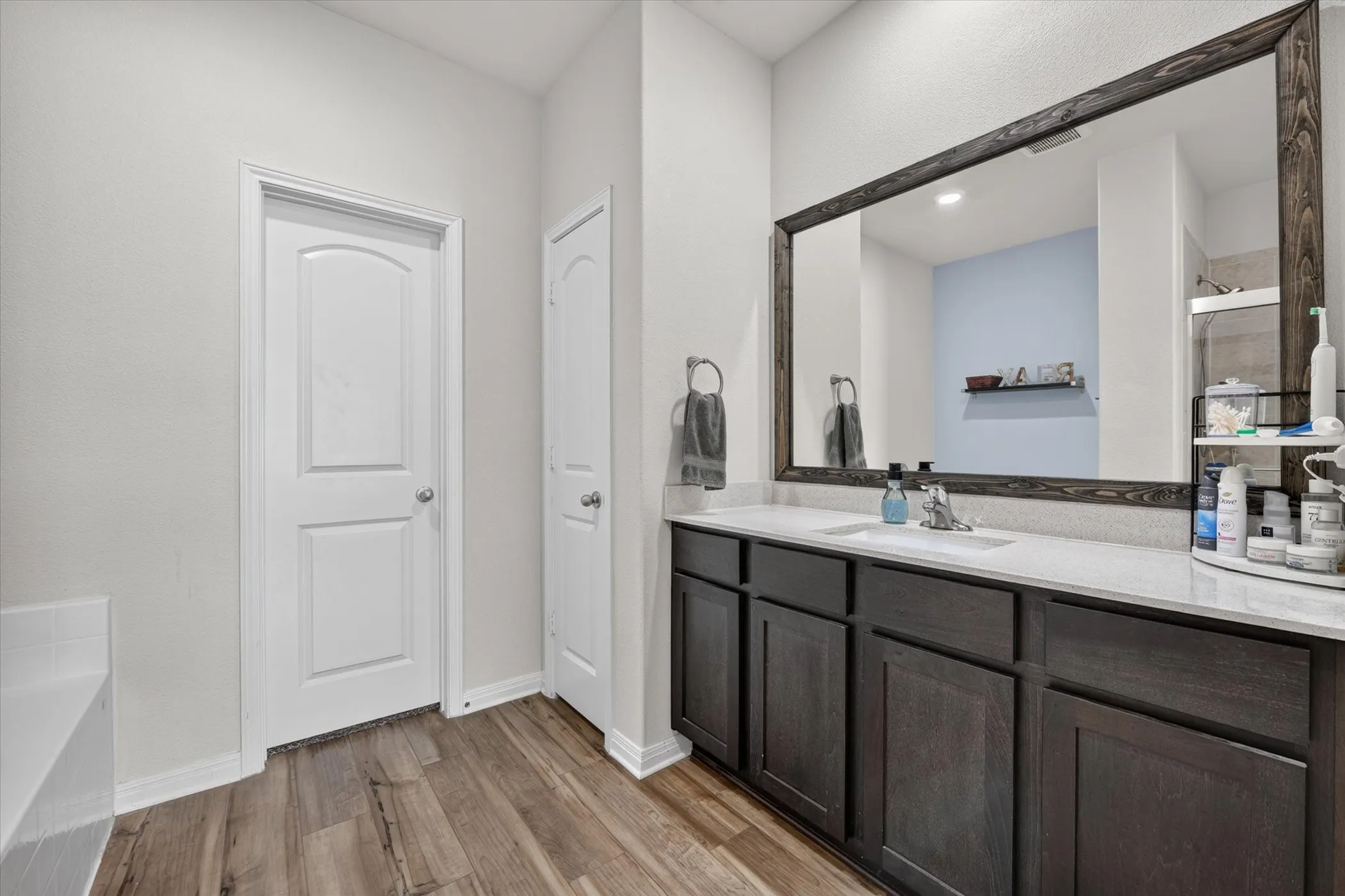 Wood-finish flooring, dark wood-finish vanity with a light countertop, and a large framed mirror