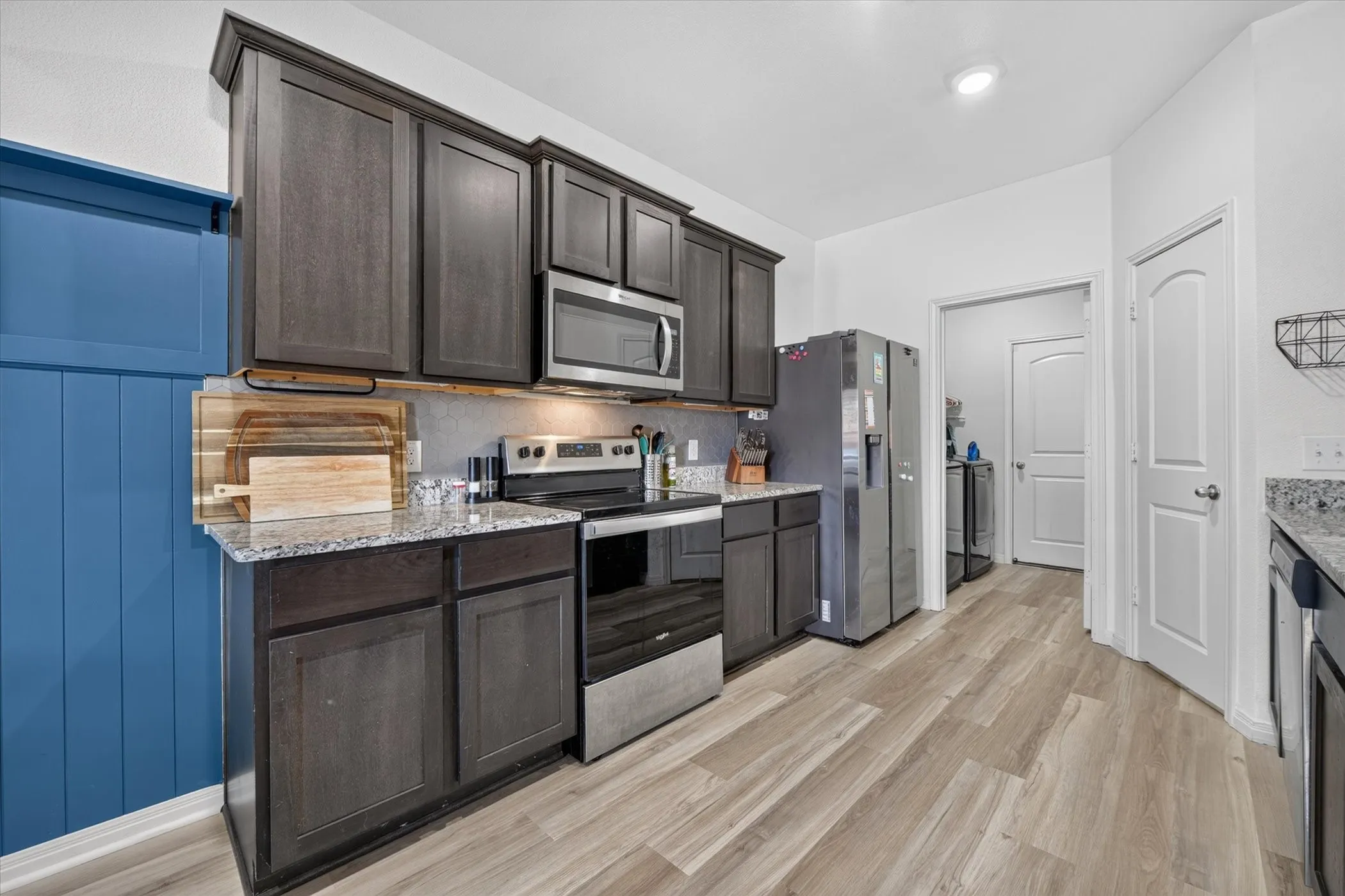 Modern kitchen featuring dark wood-finish cabinetry, stainless steel appliances, granite countertops, and wood-finish flooring