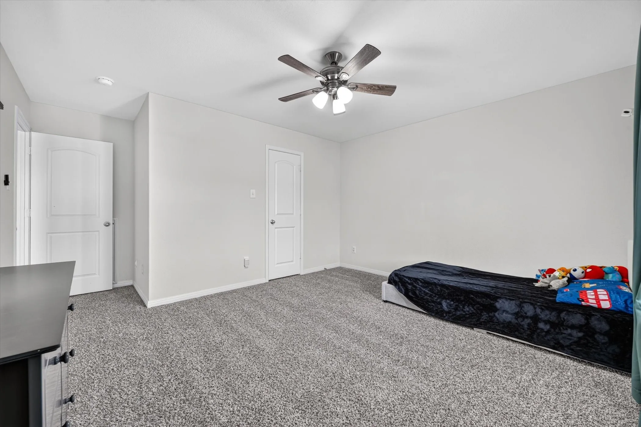 Neutral tone wall paint, textured gray carpeting, two white interior doors, and a ceiling fan with integrated lighting