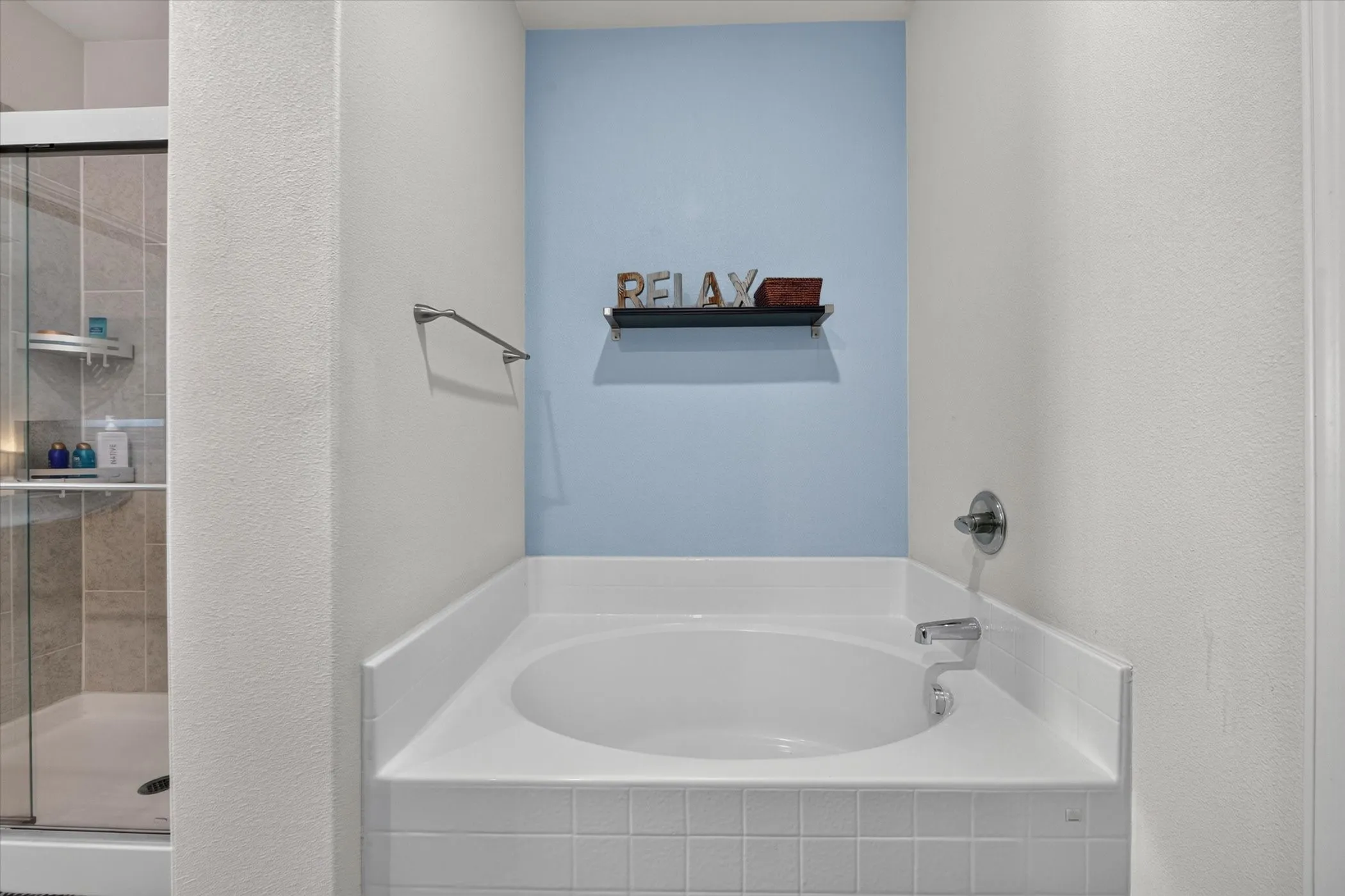 Built-in soaking tub with chrome fixtures, tiled surround, and a glass-enclosed shower with tiled walls