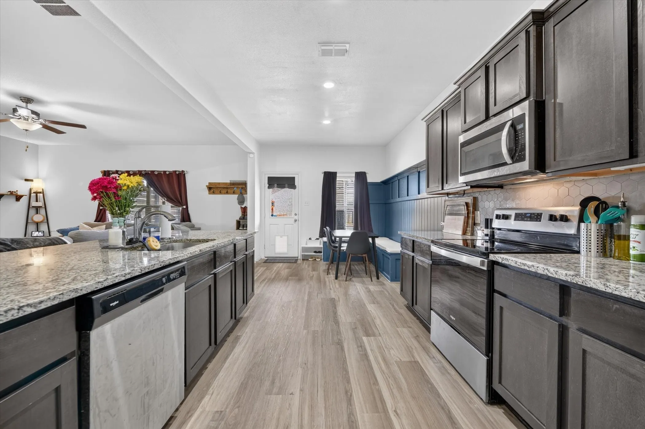 Spacious kitchen with wood-finish flooring, dark wood cabinetry, light-toned countertops, and stainless steel appliances