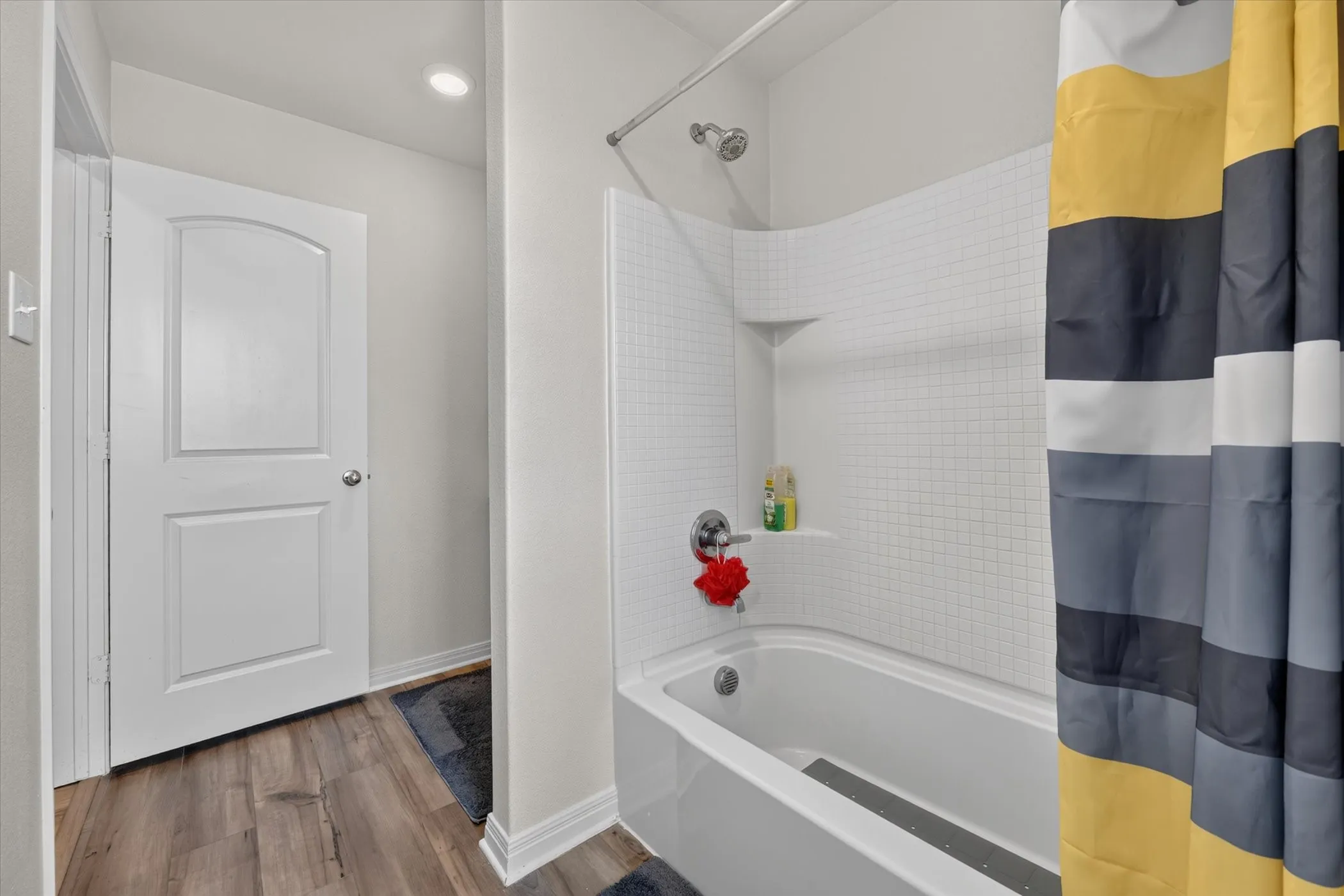 Bathtub with integrated shower, white subway tile surround, and recessed shower shelf