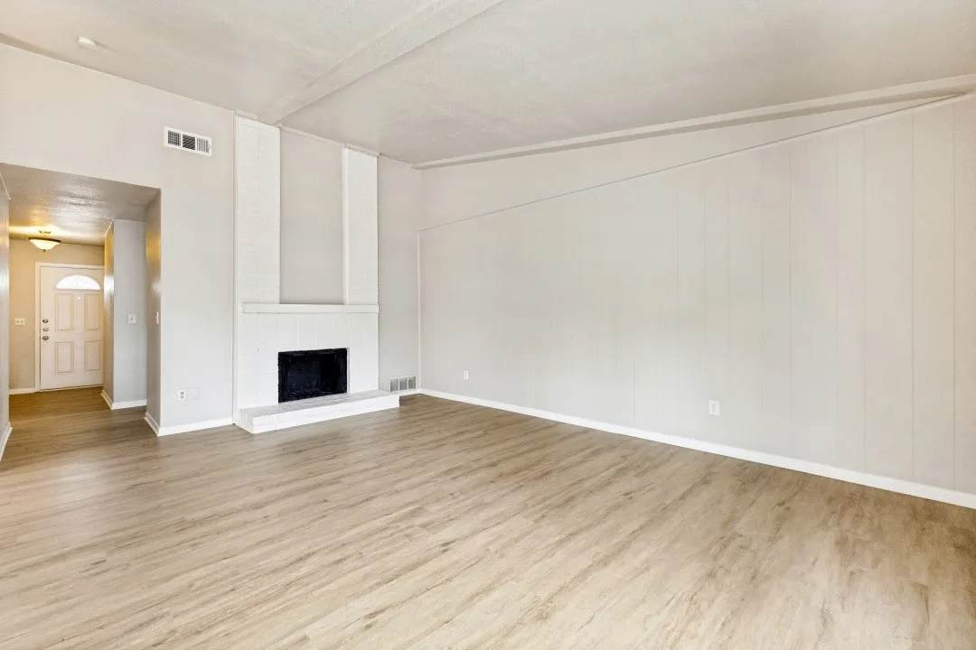 Wood-finish flooring throughout, featuring a white brick fireplace with a hearth, and panel accent wall