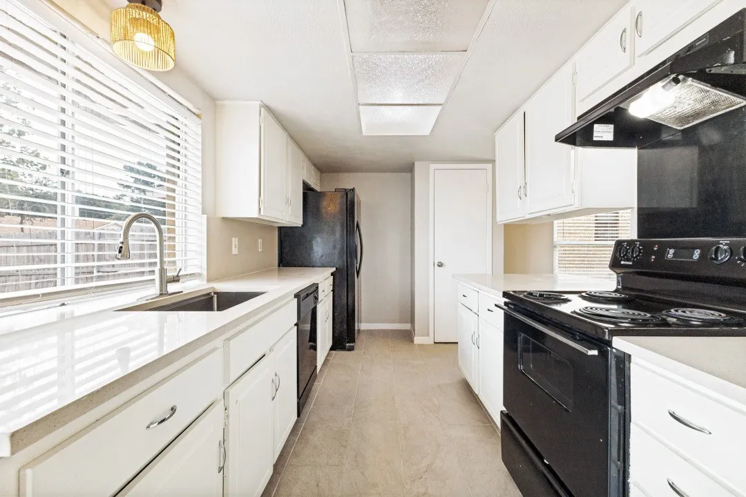 Galley kitchen featuring white cabinetry, light countertops, stainless steel sink with pull-down faucet, and black appliances