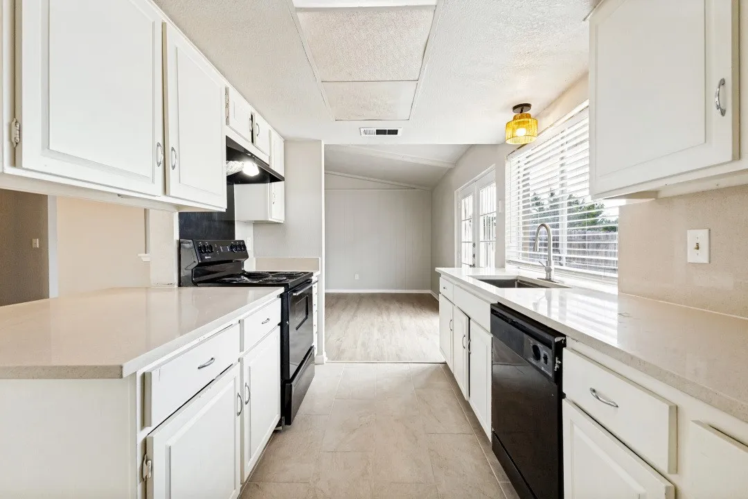 Kitchen featuring white cabinetry, light-toned countertops, tile flooring, a stainless steel sink, and a full suite of black appliances