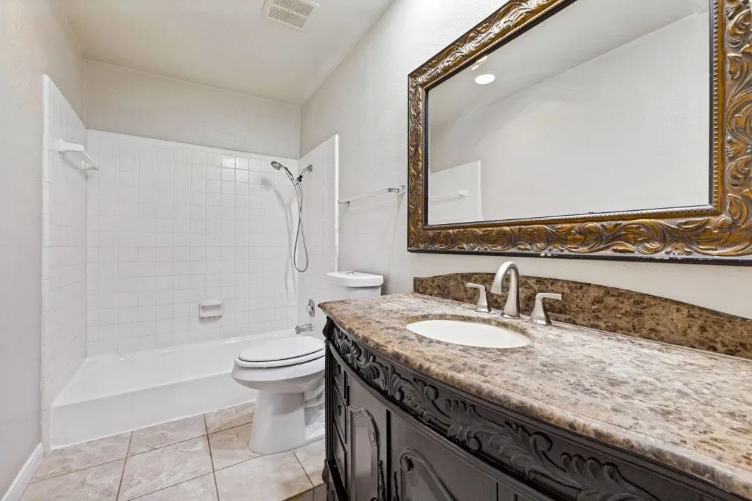 Bathroom featuring a vanity with a stone countertop, an ornate framed mirror, a built-in tub with tile surround, and tile flooring