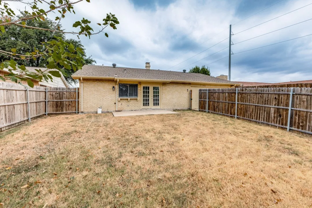 Expansive backyard featuring a full privacy fence, a concrete patio, and a brick exterior with French doors