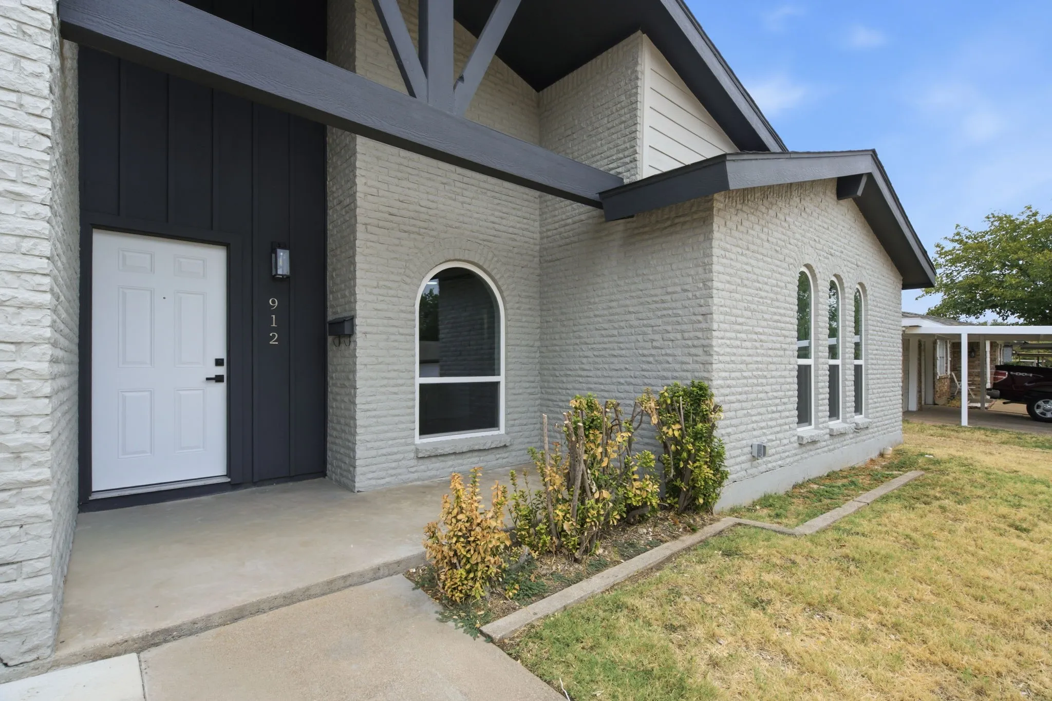 Brick exterior with arched window, carport, and concrete walkway
