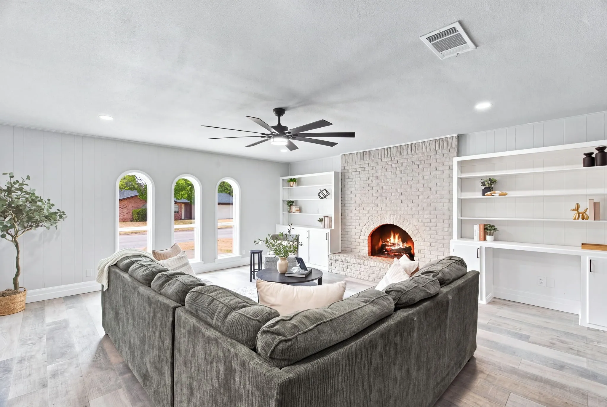 Arched windows, brick fireplace, wood-finish flooring, recessed lighting, and a ceiling fan