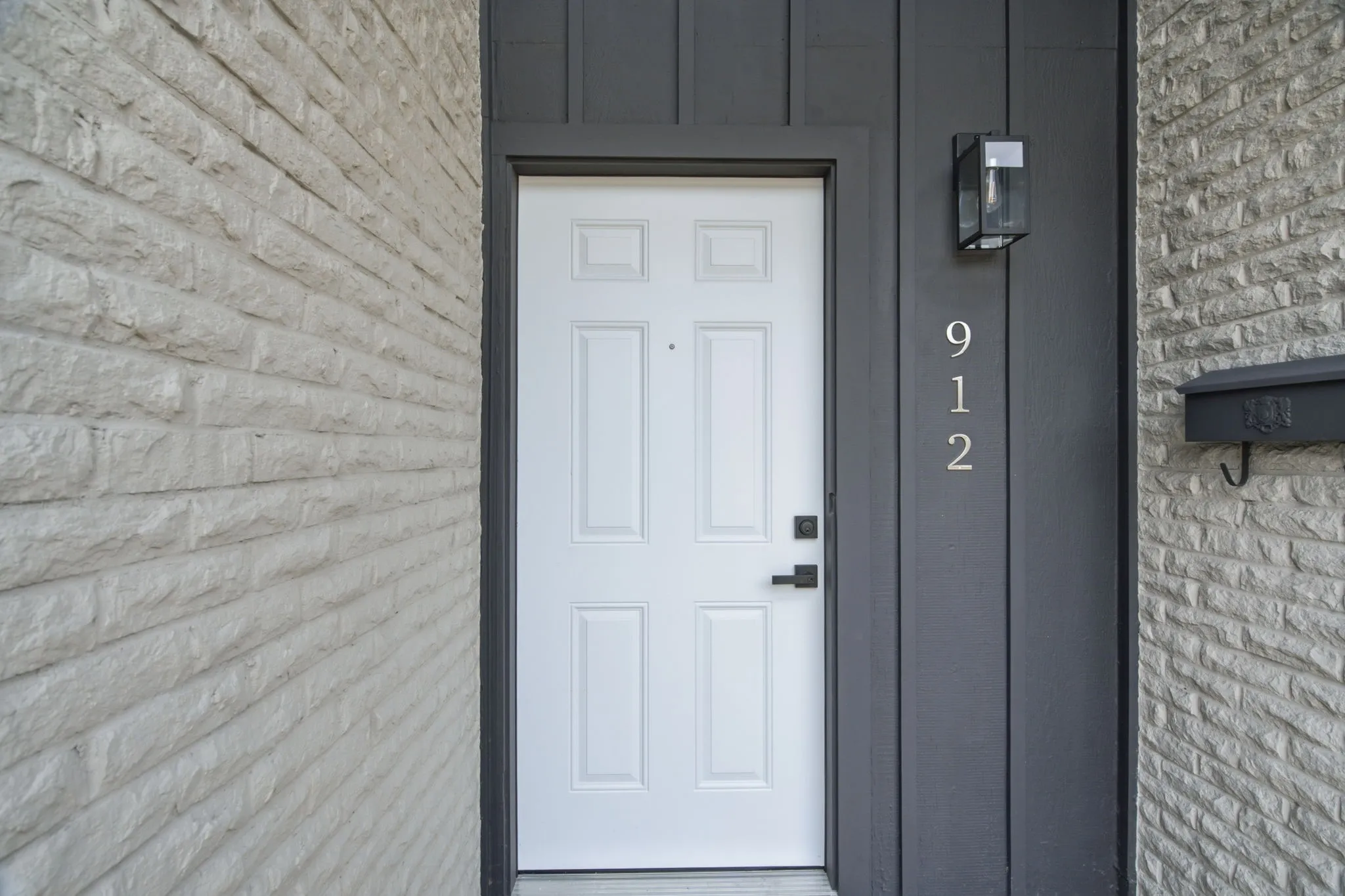 White paneled door with black hardware, flanked by gray board and batten siding and a light-colored stone-finish exterior