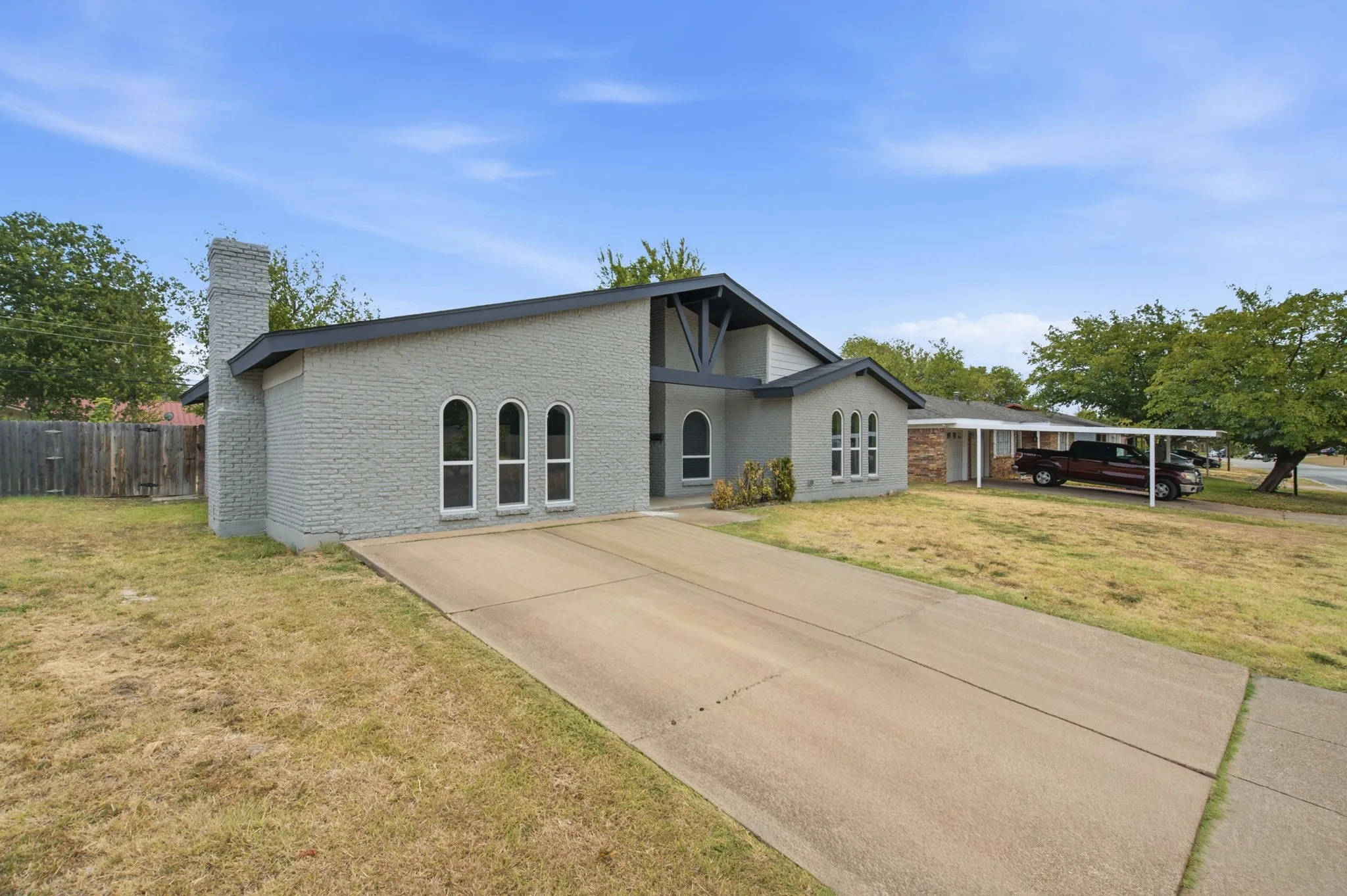 Contemporary brick exterior with arched windows, an attached carport, and a prominent chimney feature