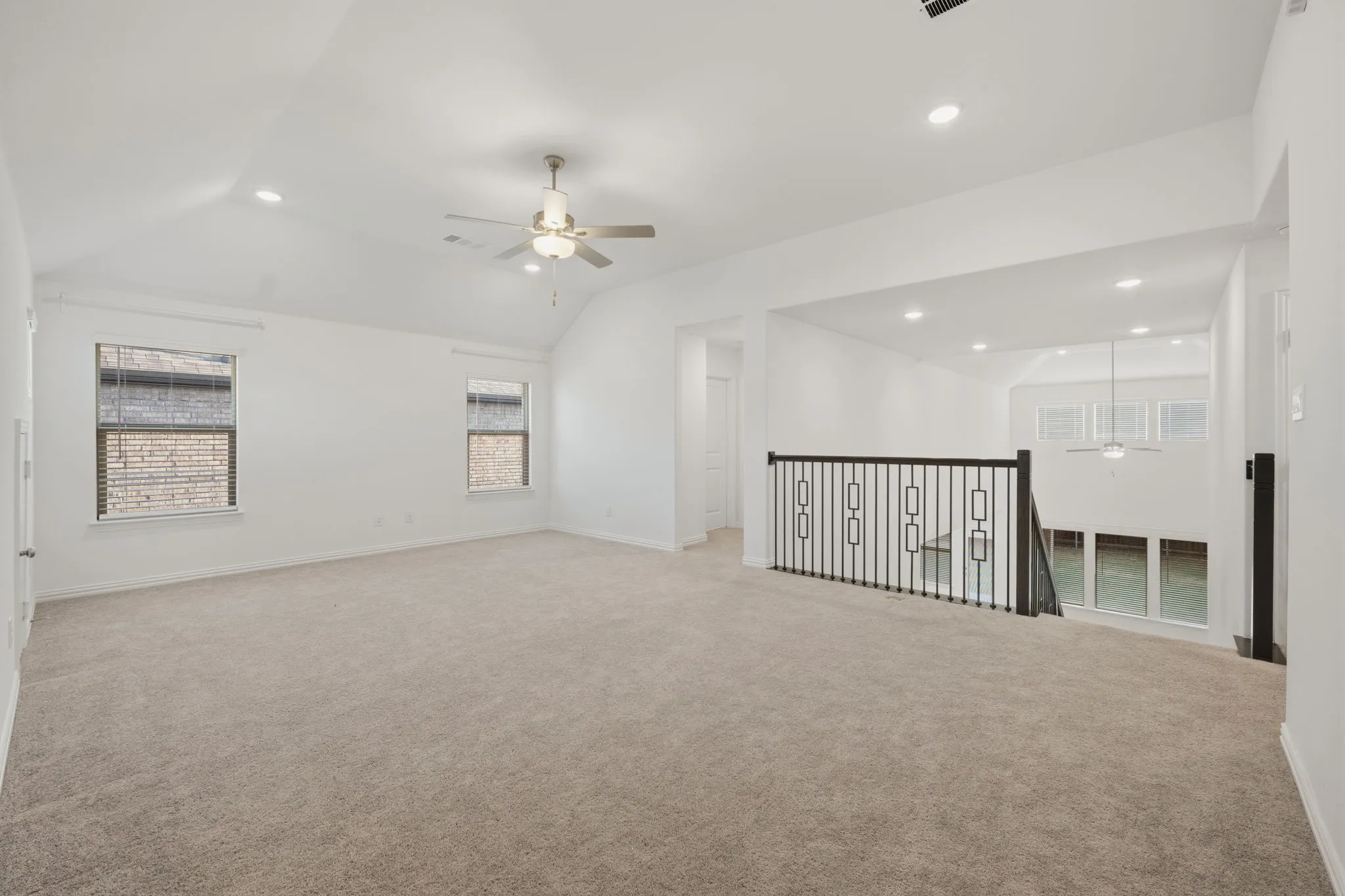 Spacious carpeted room featuring a sloped ceiling, recessed lighting, and a ceiling fan