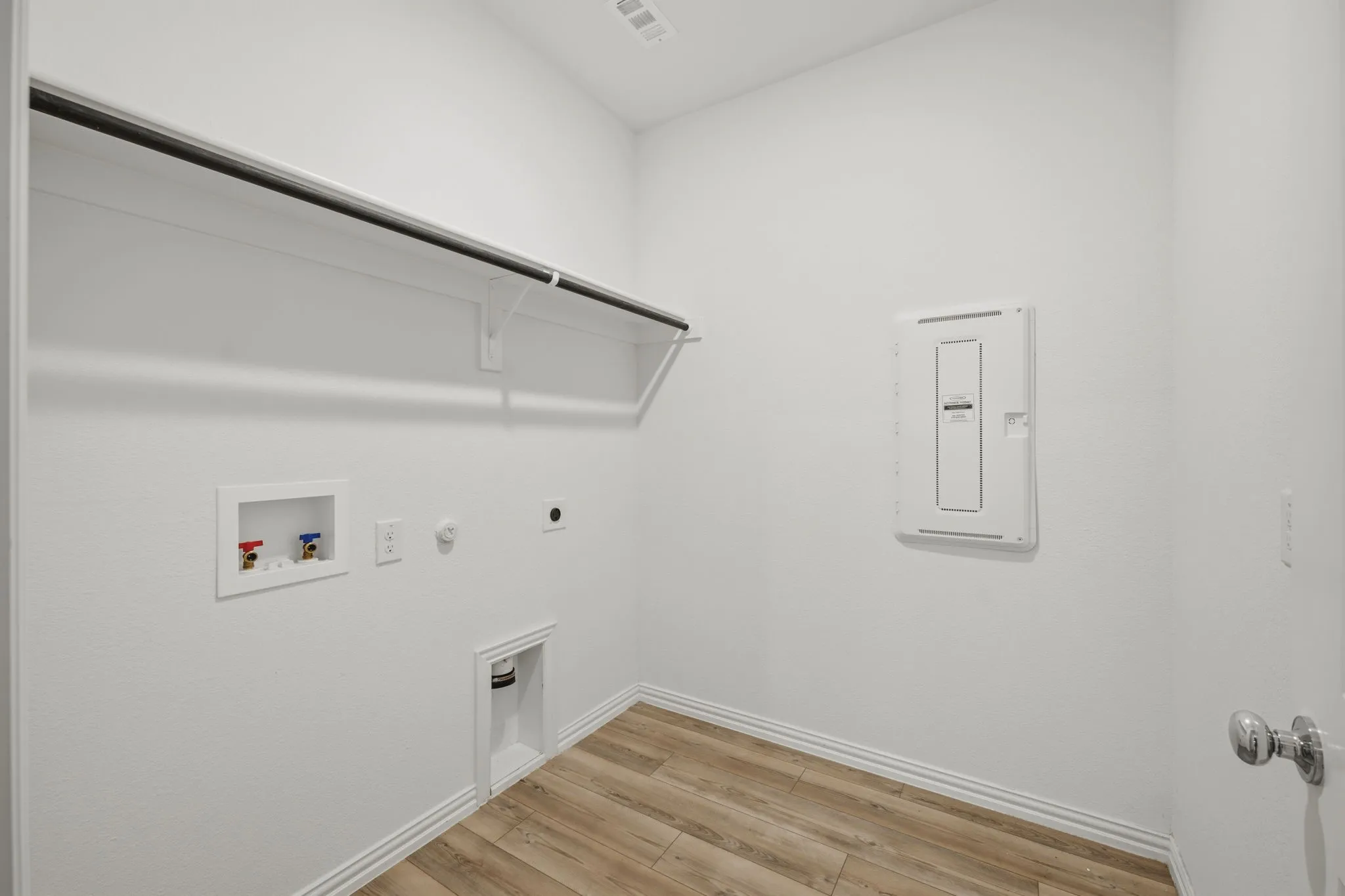 Dedicated laundry space featuring wood-finish flooring, a wall-mounted shelf, and a hanging rod