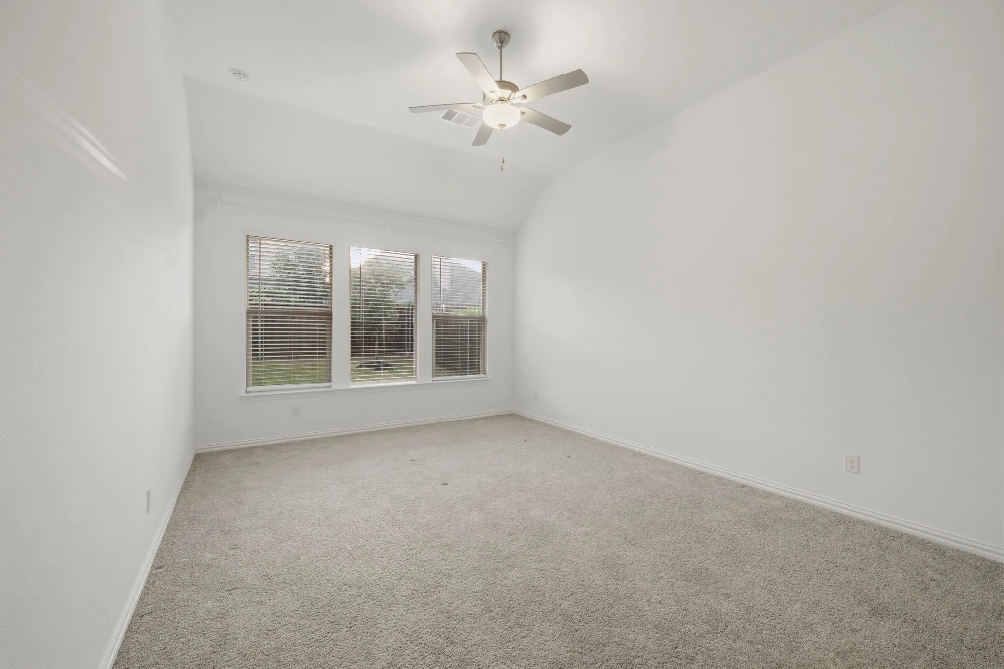 Carpeted room with vaulted ceiling, ceiling fan, and a triple window assembly with blinds