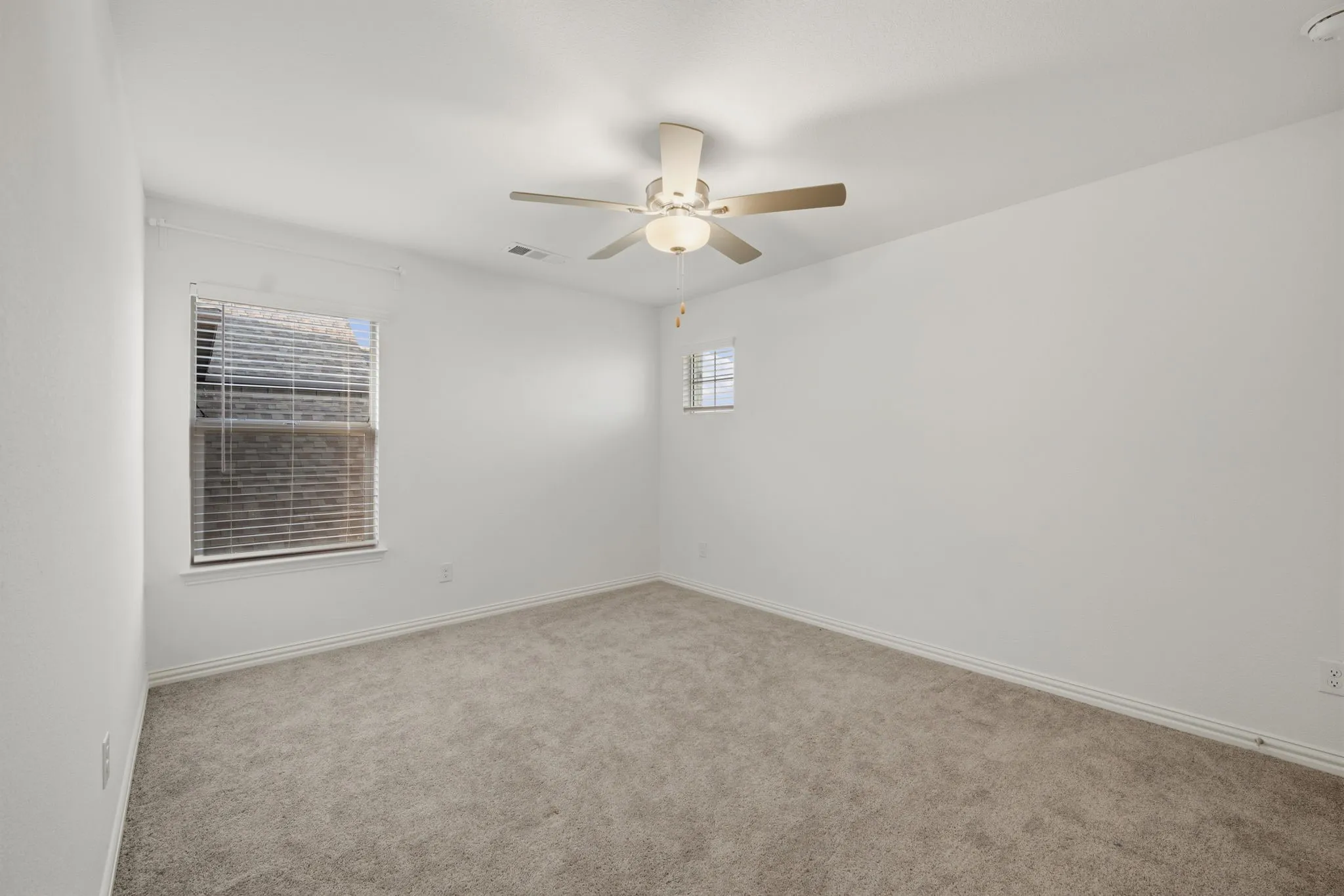 Neutral wall tones with carpet flooring, a ceiling fan with integrated lighting, and multiple windows with blinds