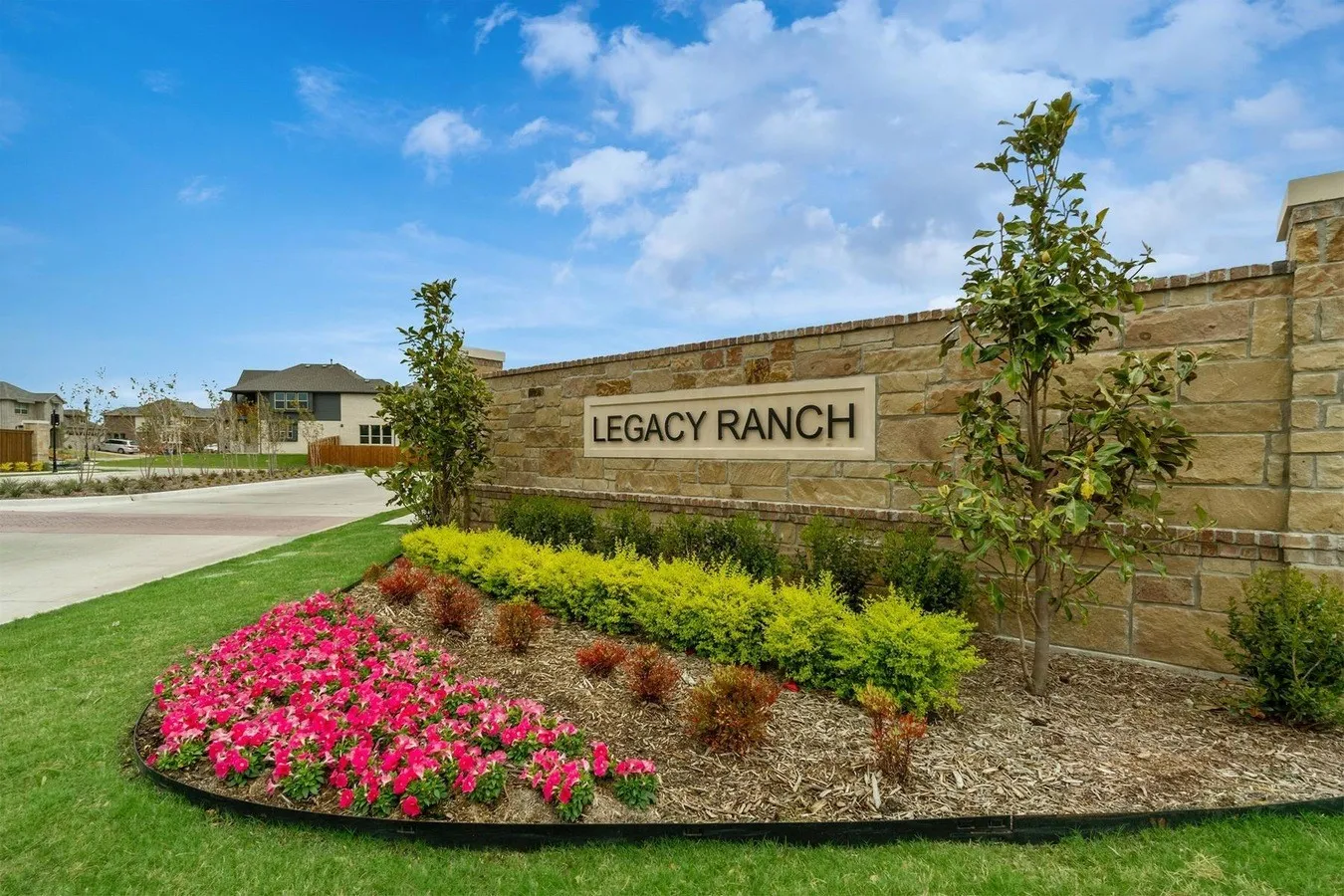 Stone entry monument with prominent signage, surrounded by mature landscaping and vibrant floral plantings