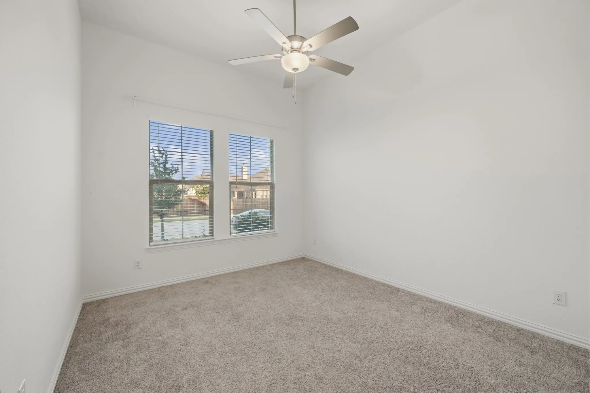 Neutral toned carpeting, dual windows with blinds, and a ceiling fan with integrated lighting