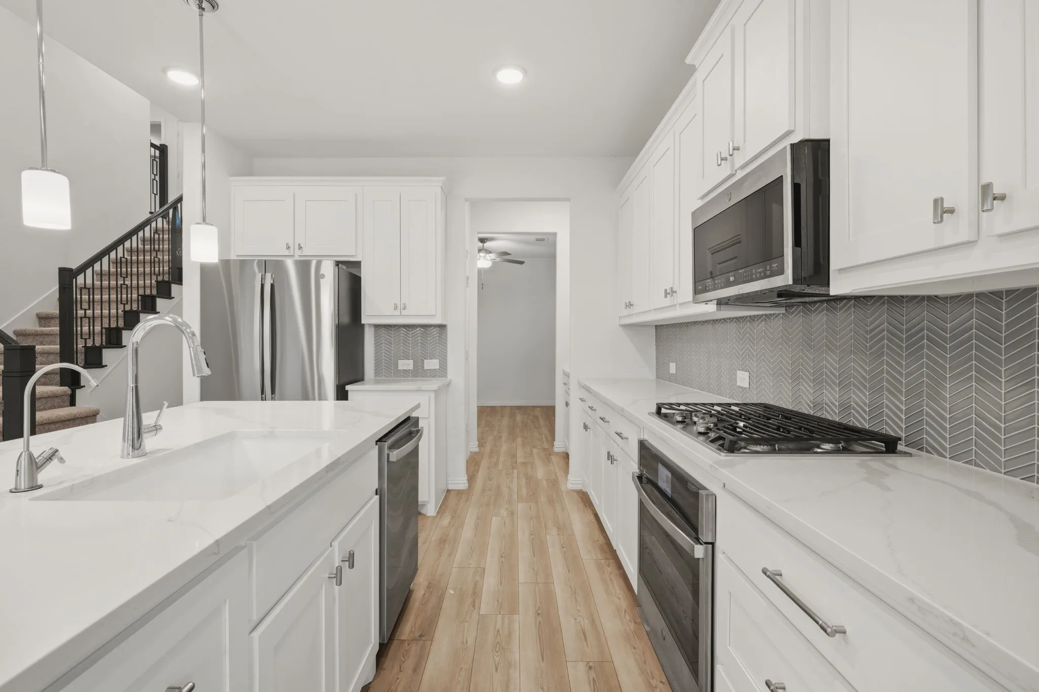Kitchen featuring light wood-finish flooring, white cabinetry, integrated stainless steel appliances, a center island with a sink, and a chevron-patterned tile backsplash