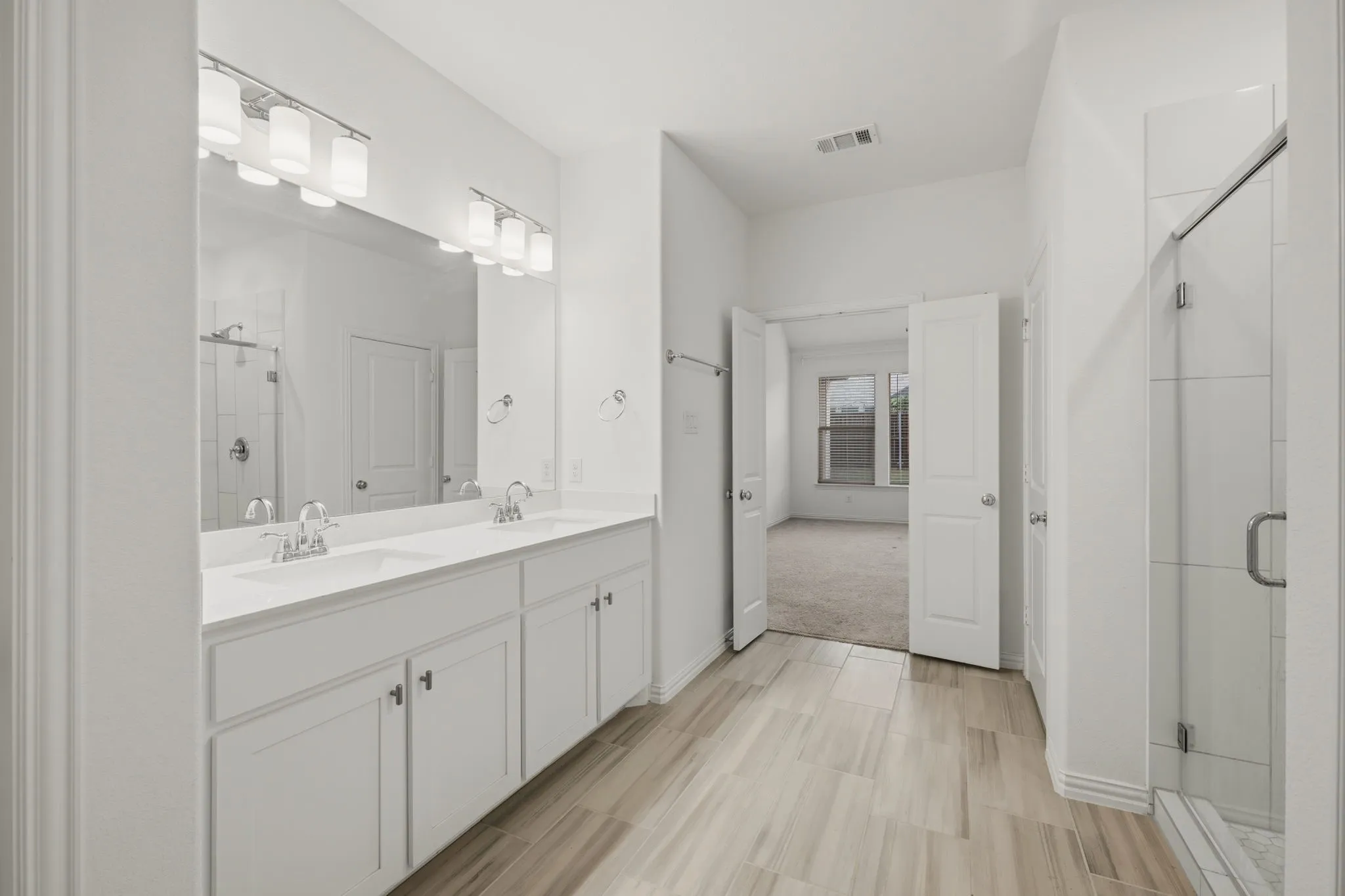 Dual vanity with undermount sinks, wood-finish tile flooring, walk-in shower with glass enclosure, and white cabinetry with brushed nickel hardware