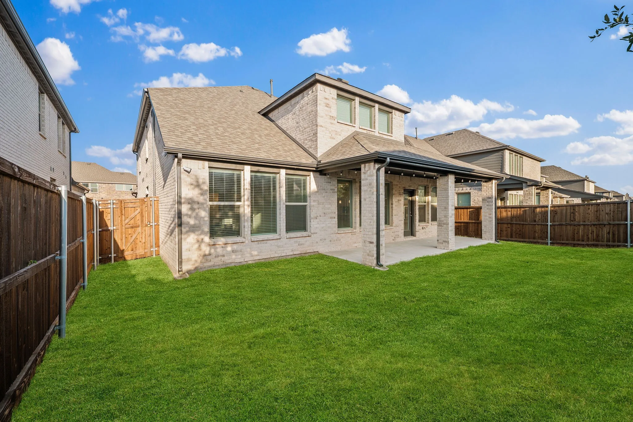 Expansive backyard featuring a lush lawn, privacy fencing, a covered patio, and brick exterior