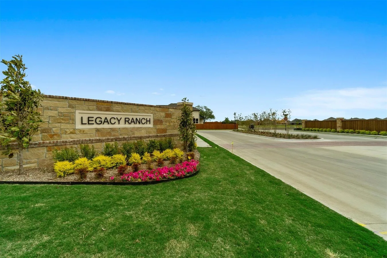 Stone entryway with integrated signage, vibrant planted landscaping, and manicured lawns