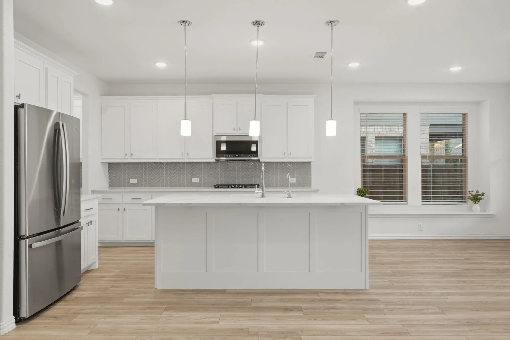 Open concept kitchen featuring an expansive island, white cabinetry, stainless steel appliances, and wood-finish flooring