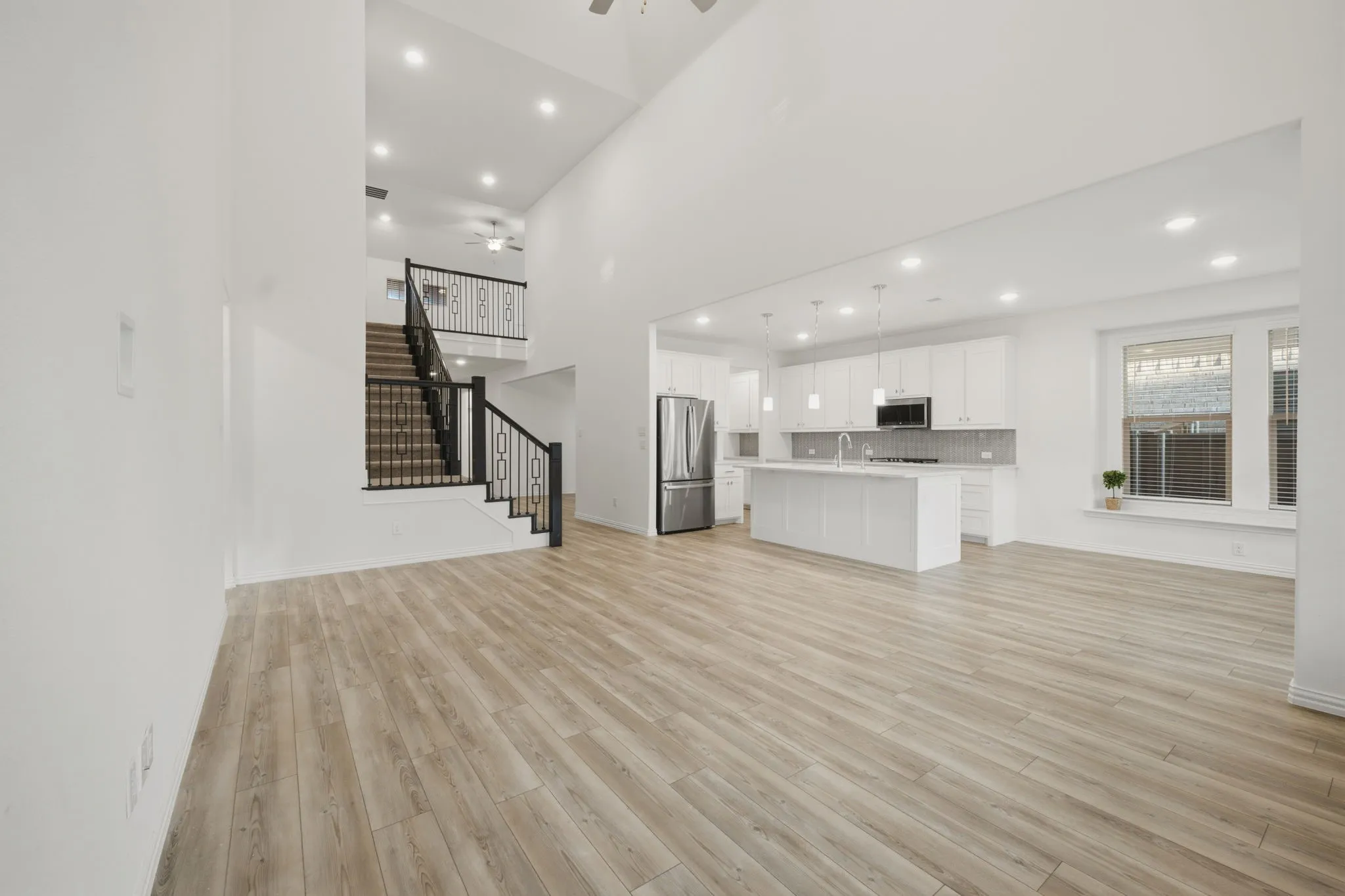 Vaulted ceilings with recessed lighting, wood-finish flooring, a contemporary kitchen with a large island, stainless steel appliances, and a staircase with decorative wrought iron railings