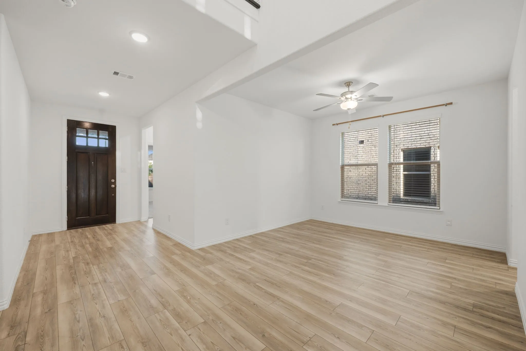 Wood-finish flooring throughout, framed windows, ceiling fan, recessed lighting, and a dark wood entry door with glass panels