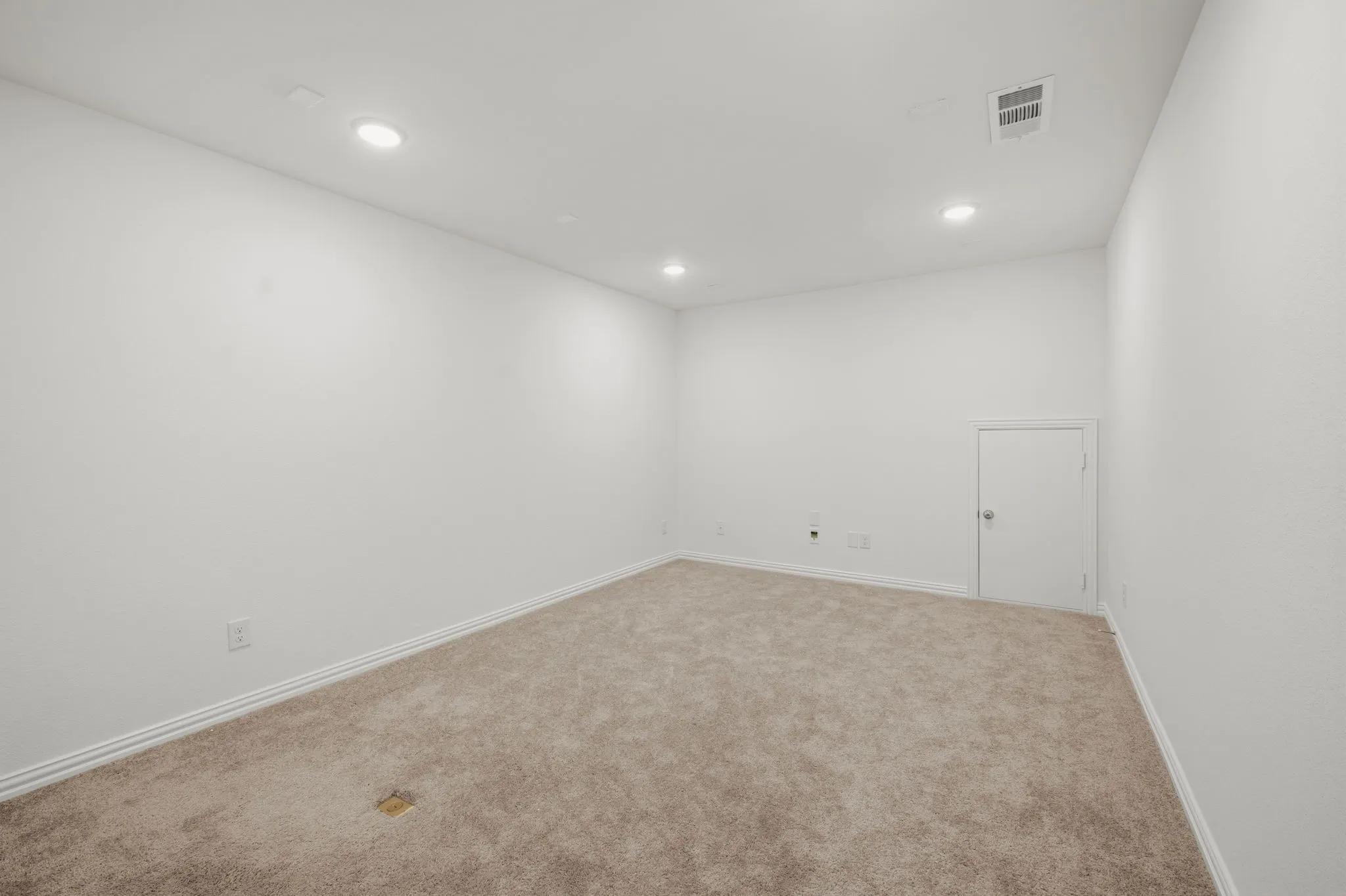 Recessed ceiling lighting, textured white walls, neutral carpeting, and a white interior door