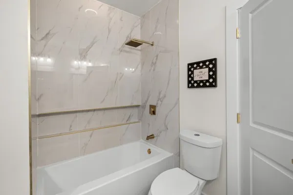 Bathtub with marble-look tile surround, shower niche, and gold-finish fixtures