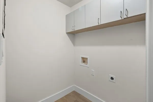 Built-in overhead white cabinetry with silver hardware, wall-mounted utility hookups, and wood-finish flooring