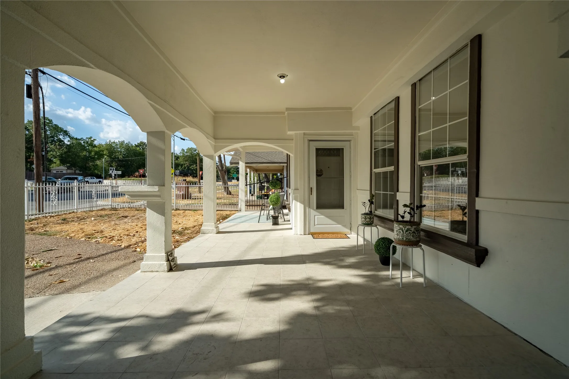 Expansive covered porch with light-toned tile flooring, supporting columns, and arched openings